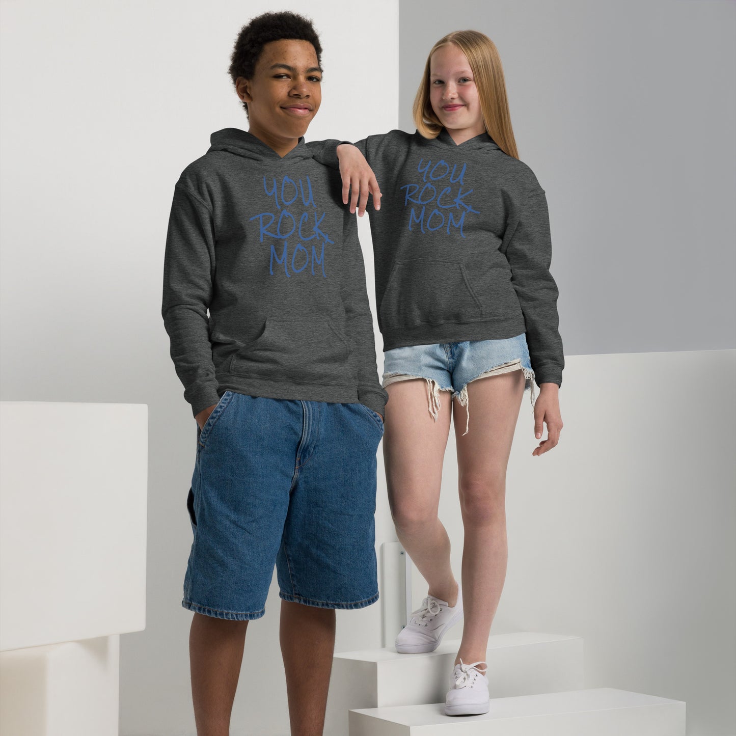 Two children wearing gray hoodies with 'You Rock Mom' text, standing on a white platform.