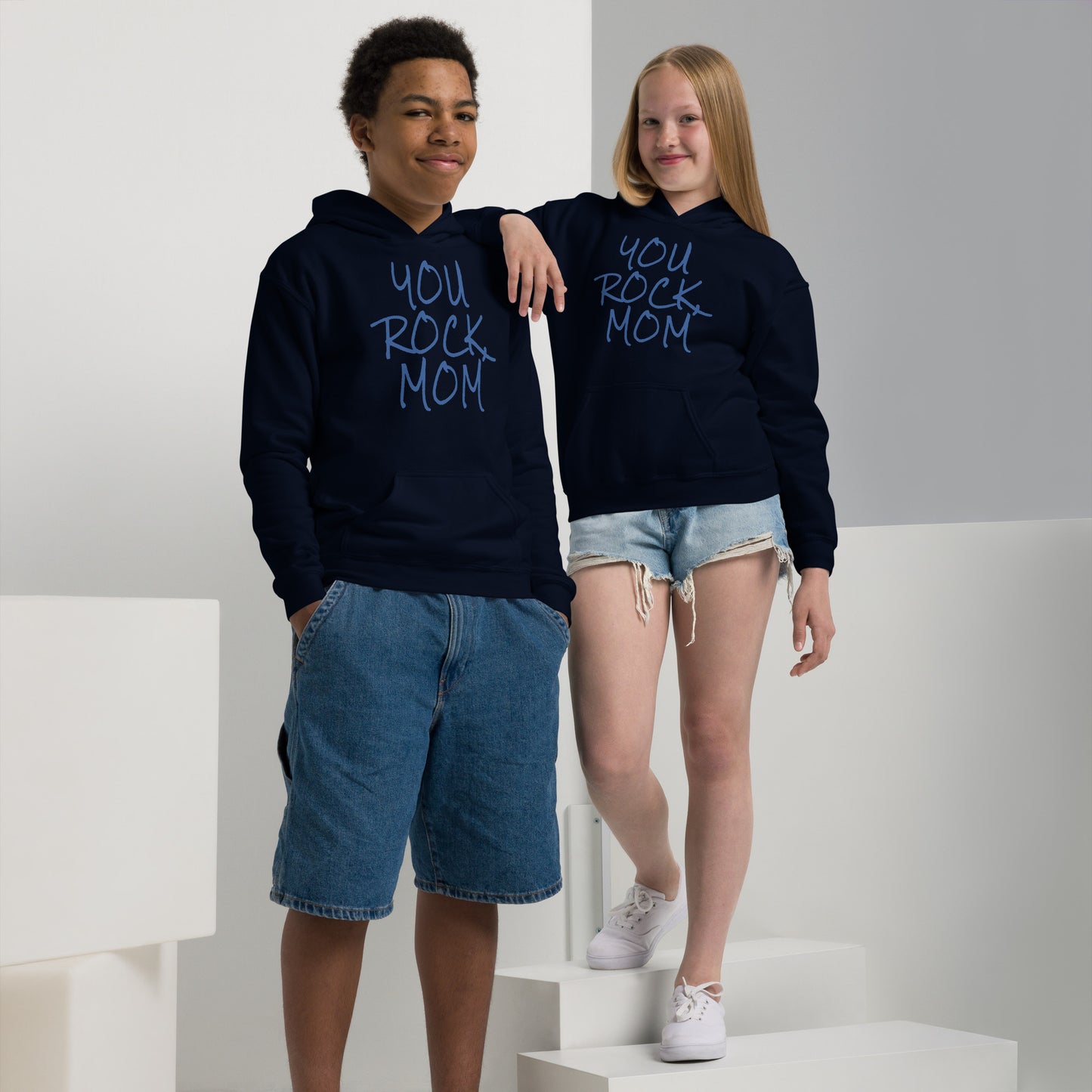 Two children wearing navy blue hoodies with 'You Rock Mom' text, standing on a white platform.