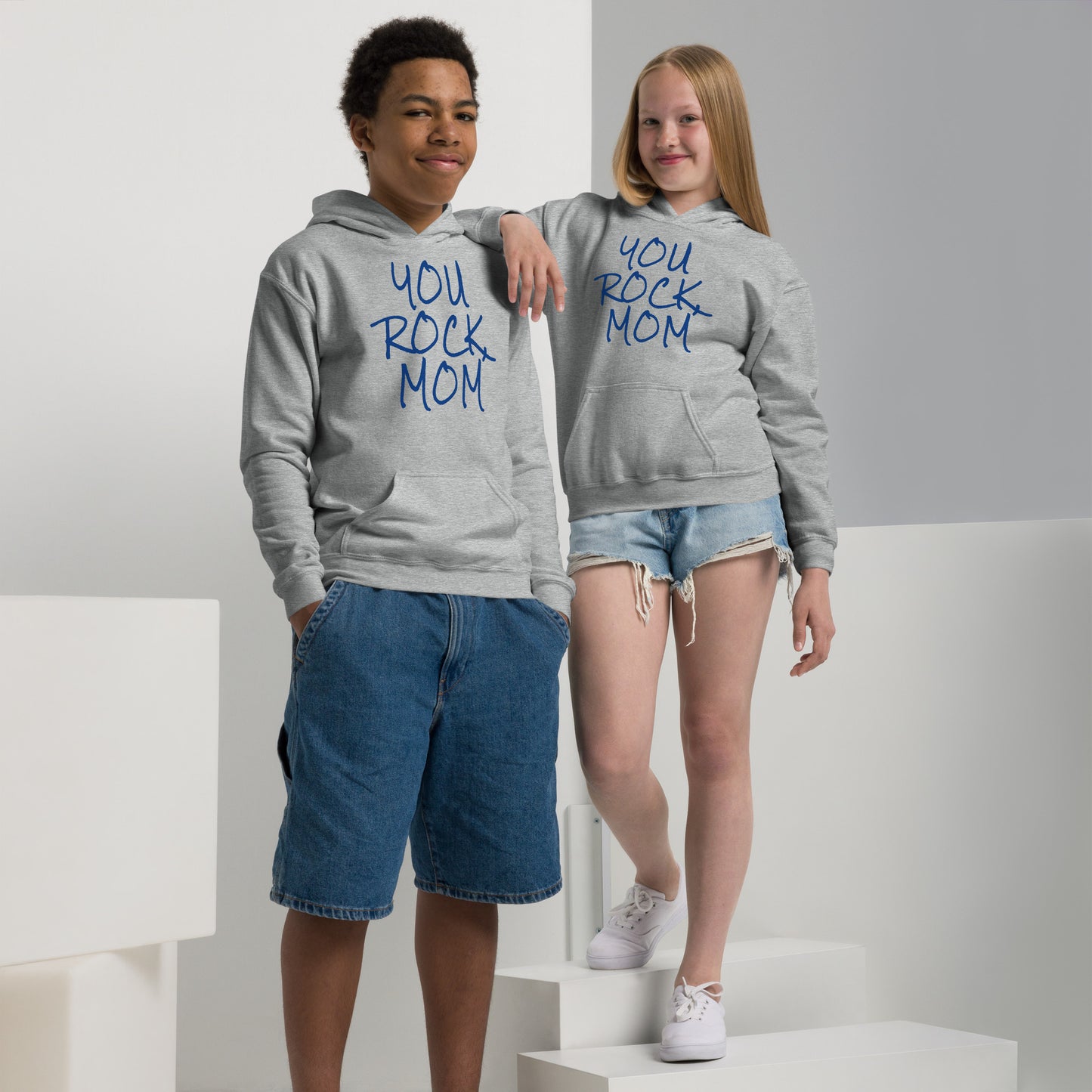 Two children wearing gray hoodies with 'YOU ROCK MOM' text, standing on a white platform.