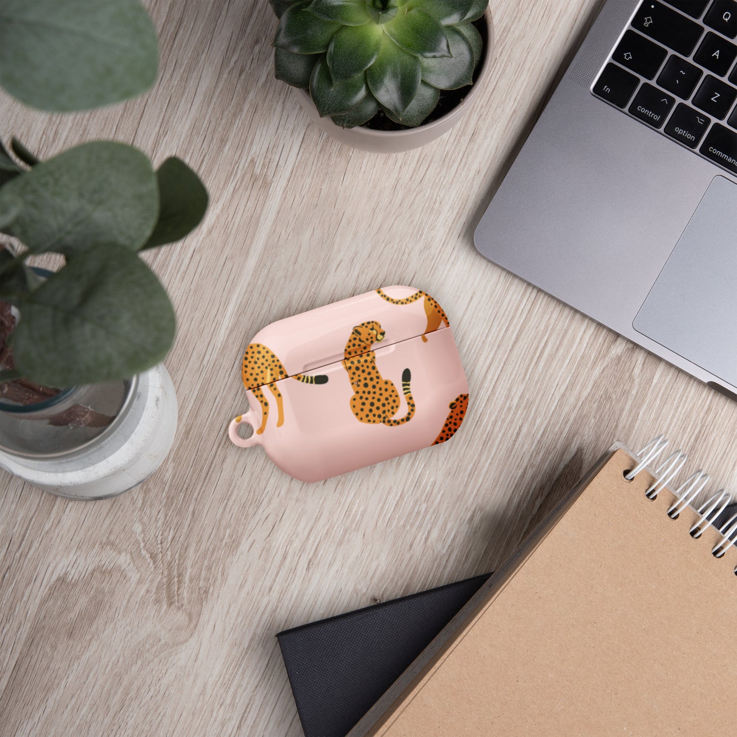 Pink case with leopard print on a wooden desk with laptop, notebook, and plants.