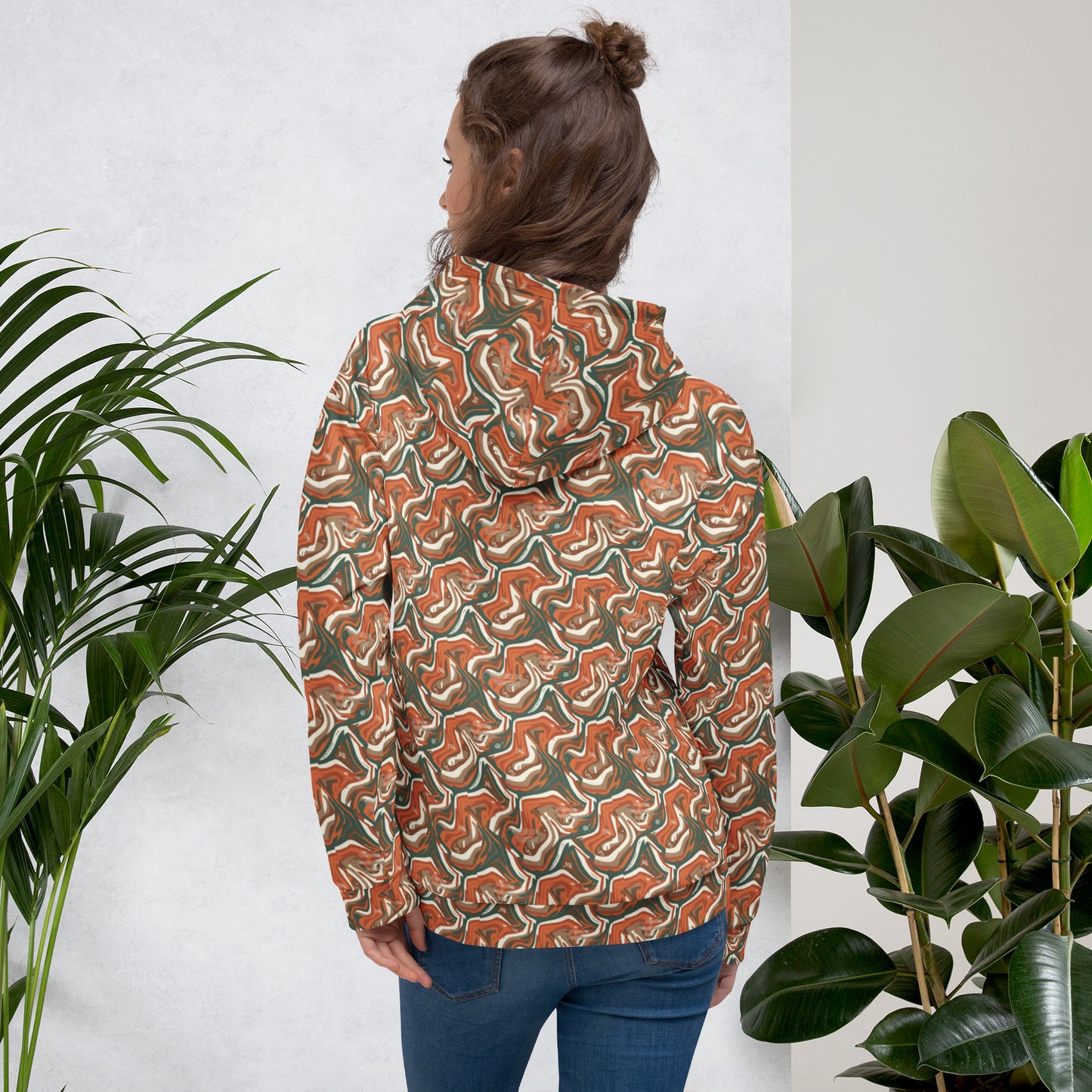 Person wearing a patterned jacket standing between two plants against a white wall