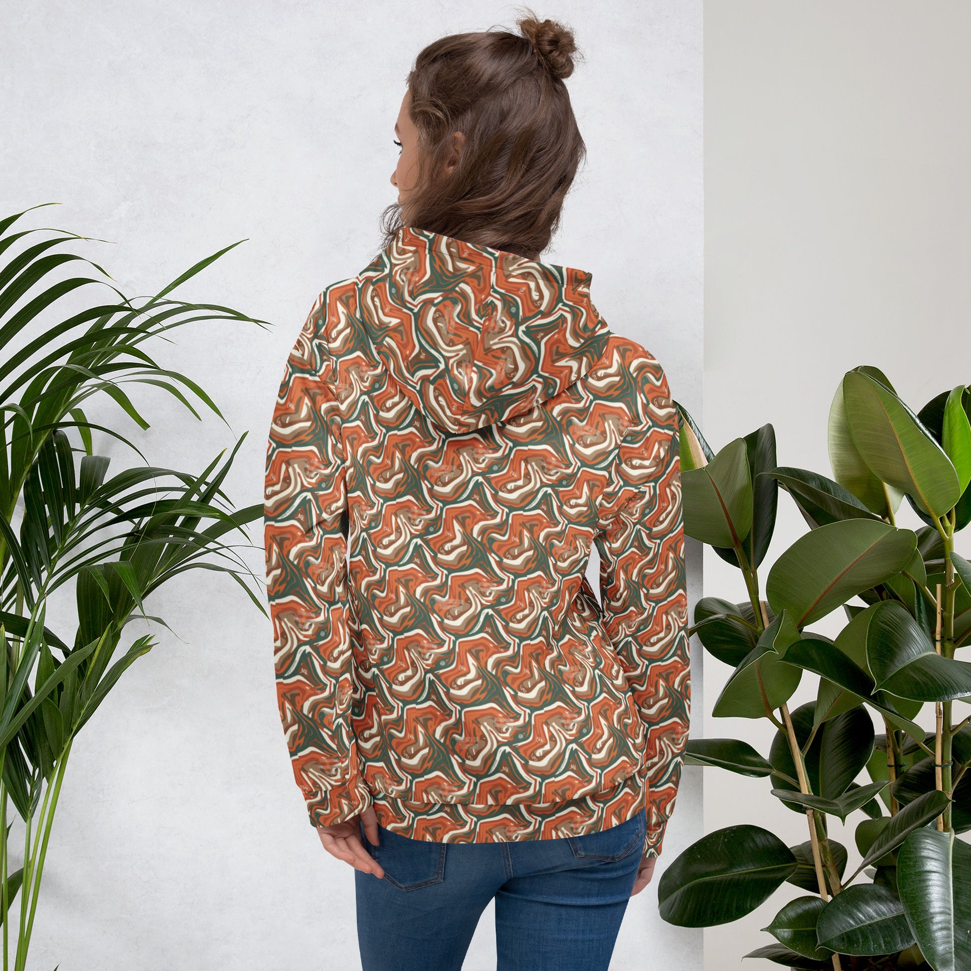 Person wearing a patterned jacket standing between two plants against a white wall