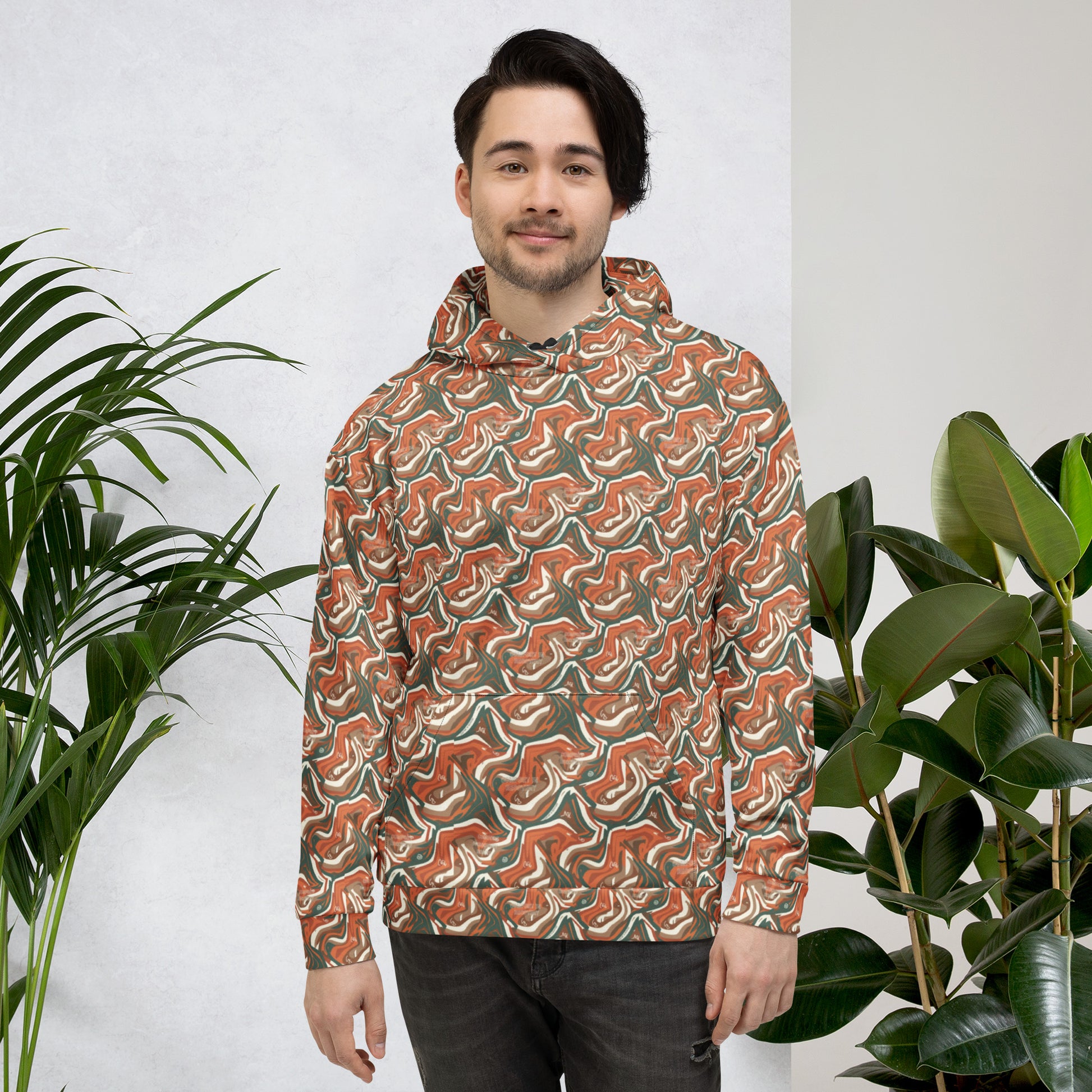 Man wearing a patterned jacket standing between two plants against a white wall