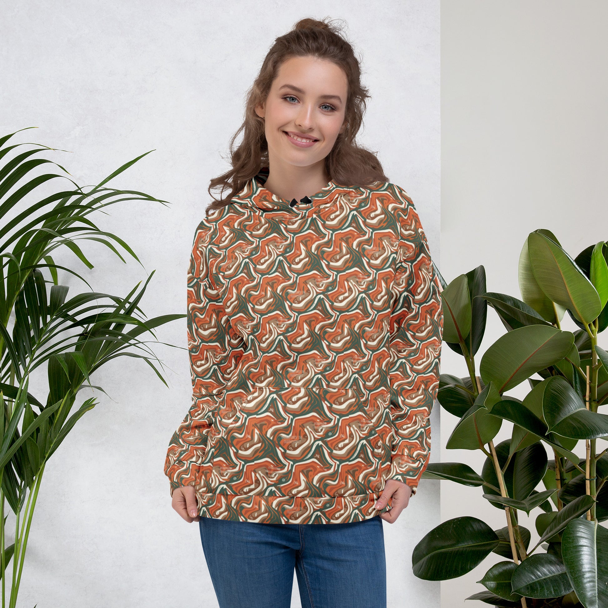 Woman wearing a patterned shirt standing between two plants against a white wall