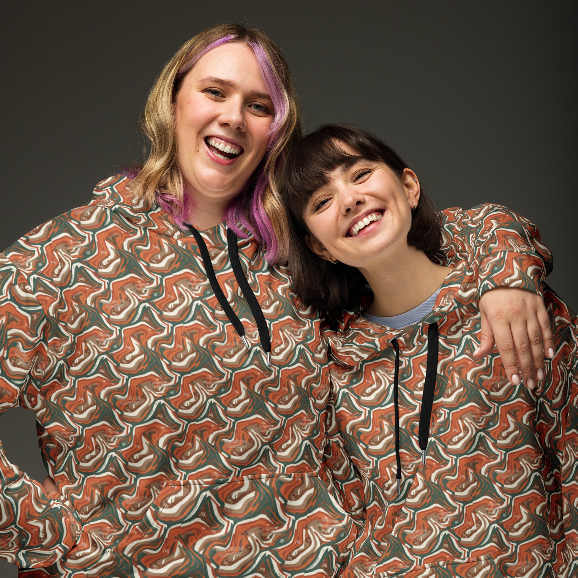 Two people wearing patterned hoodies against a dark background