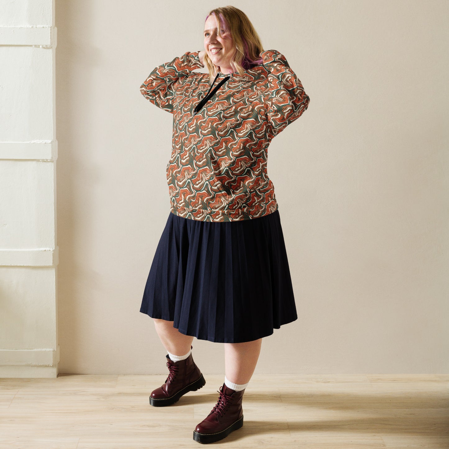 Woman wearing a patterned top and navy skirt with burgundy boots indoors.