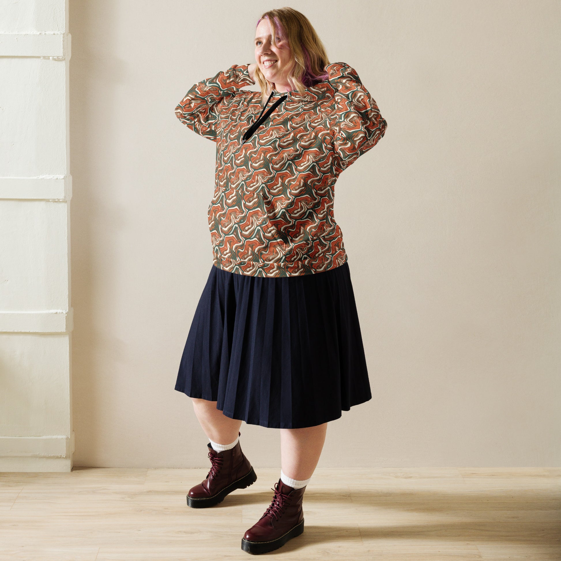 Woman wearing a patterned top and navy skirt with burgundy boots indoors.