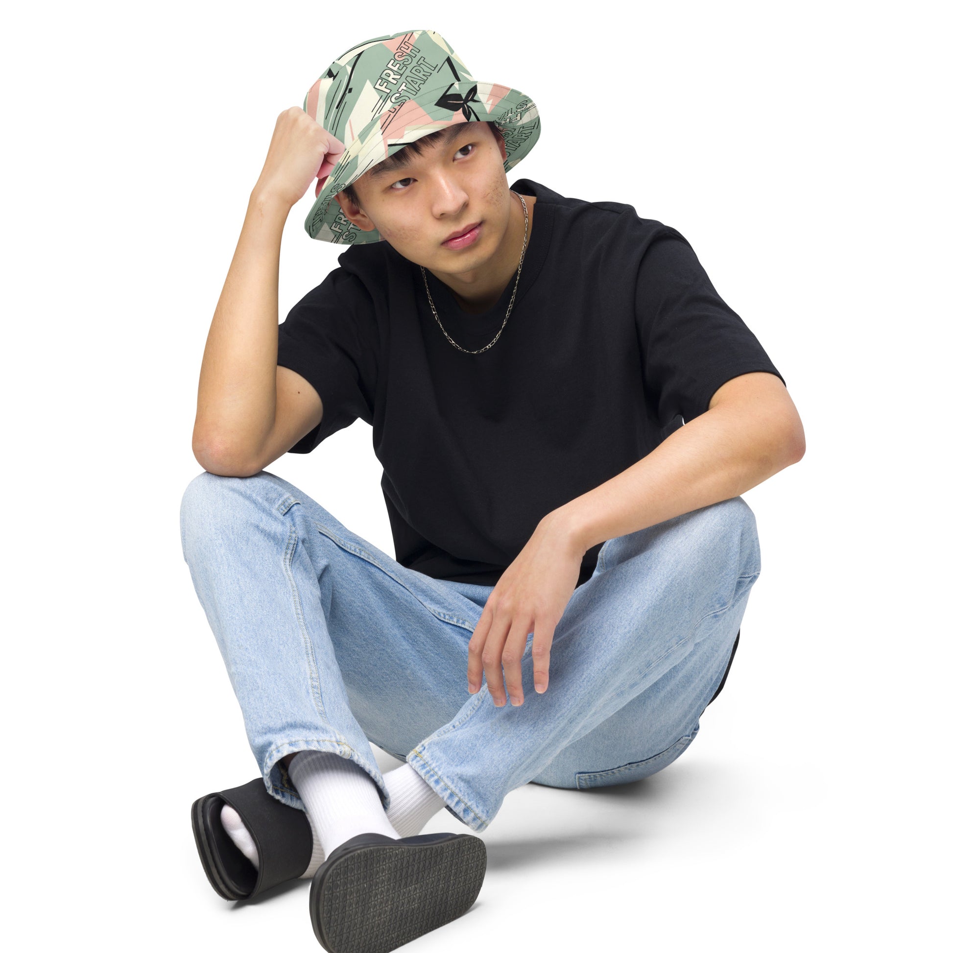 Person wearing a black t-shirt, light blue jeans, and a patterned bucket hat on a white background