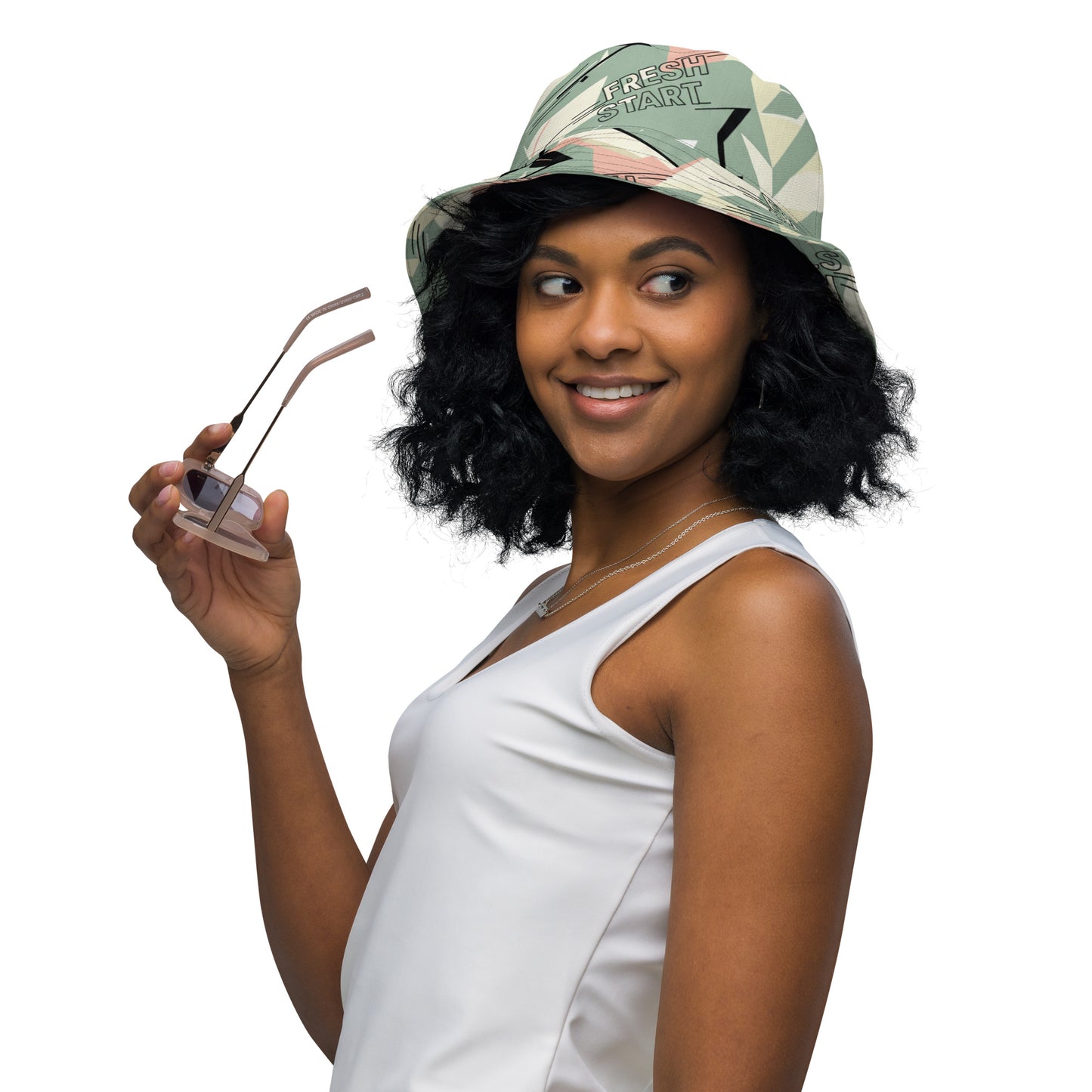 Woman wearing a white sleeveless top and colorful cap holding sunglasses on a white background