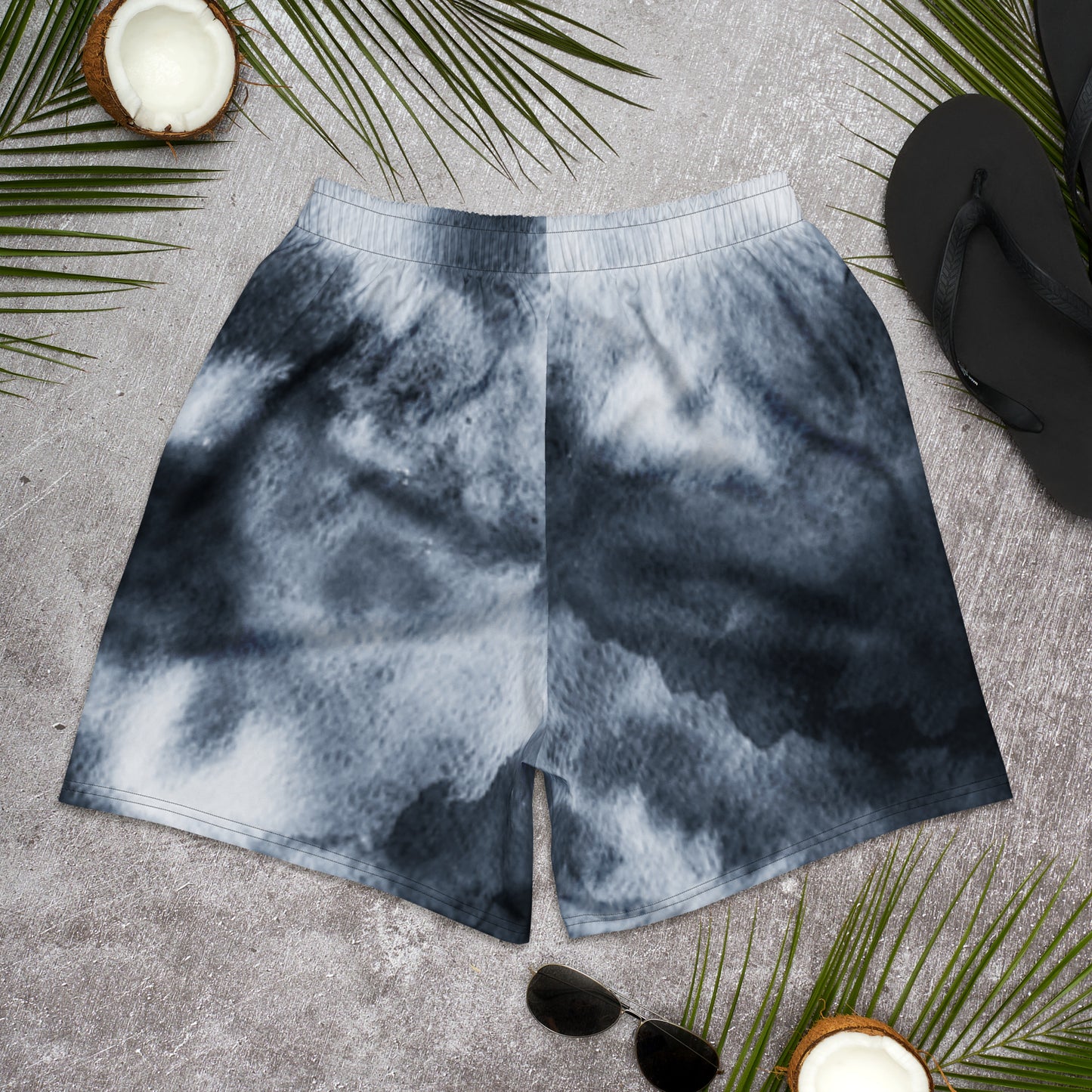 Tie-dye shorts on a textured surface with palm leaves and sunglasses.