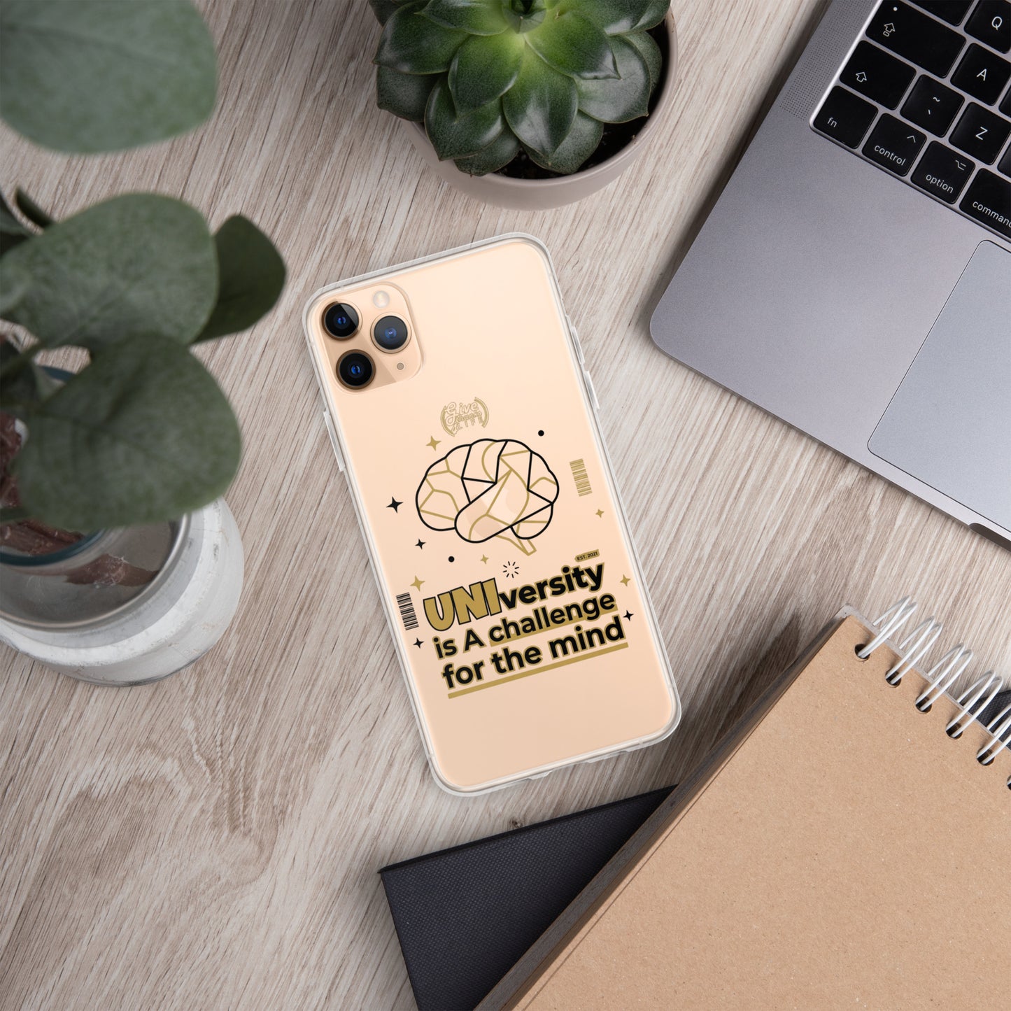 Phone case with 'University is a challenge for the mind' design on a desk with laptop and plants
