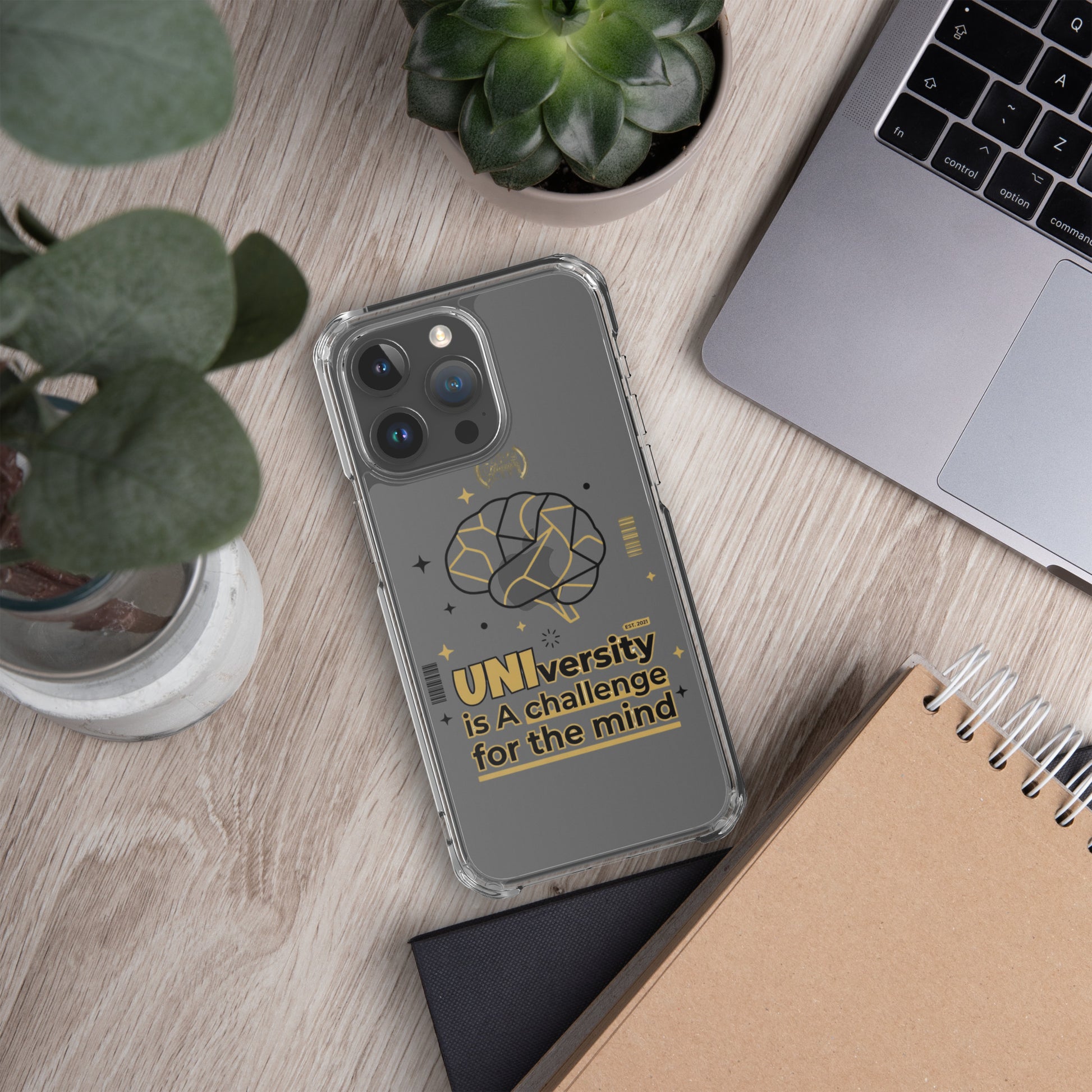 Phone case with 'UNI'versity is a challenge for the mind design on a desk with plants and a laptop.