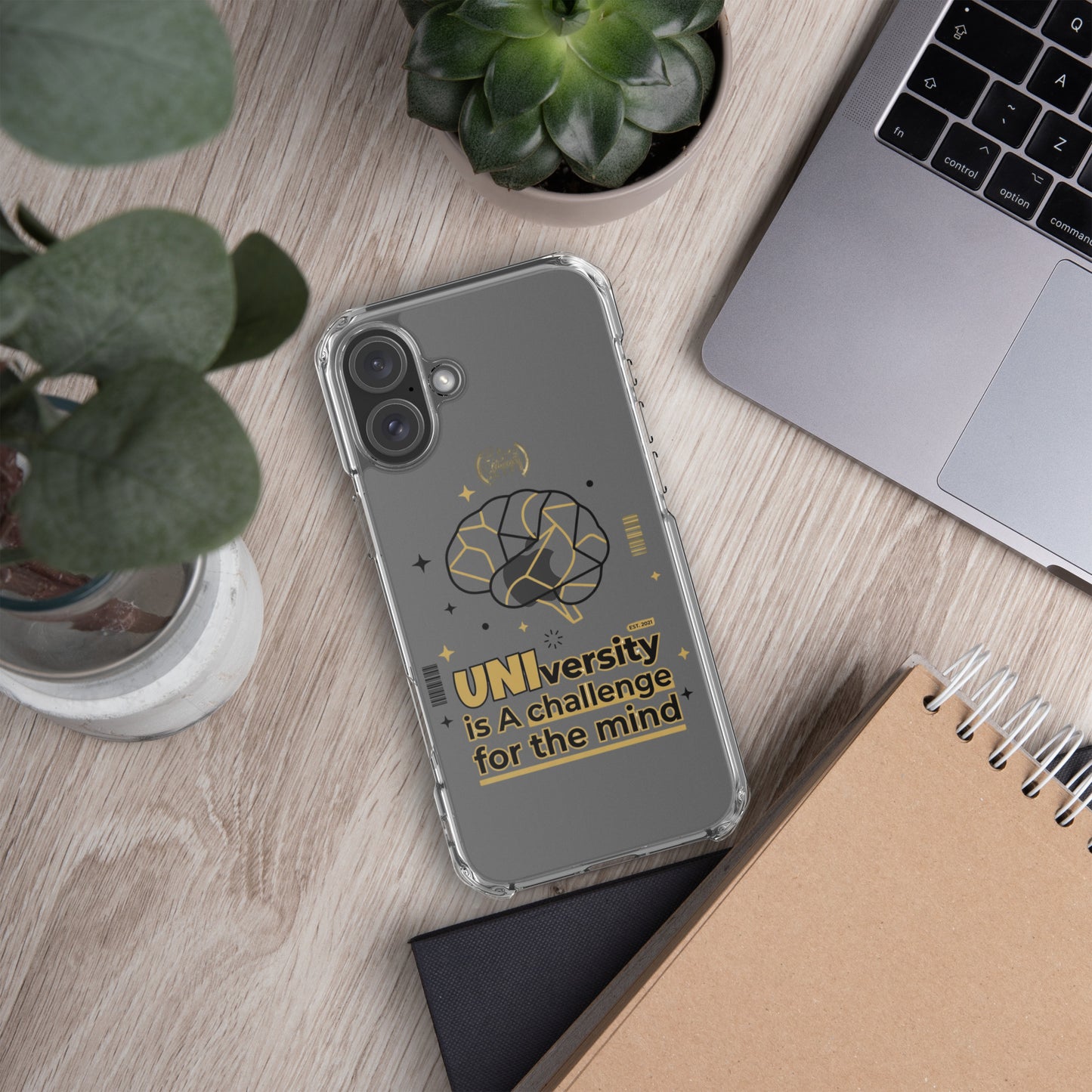 Phone with a clear case on a desk with laptop, notebook, and plants
