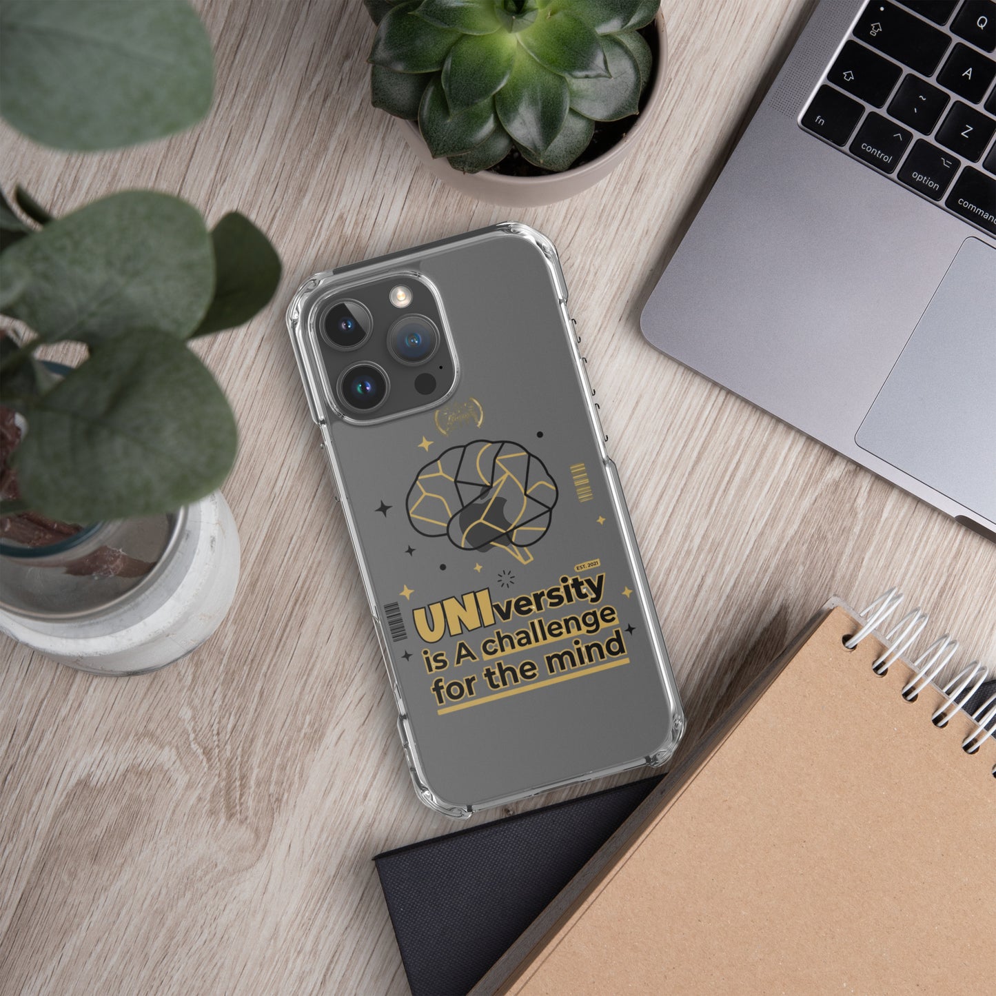 Phone case with 'UNI'versity is a challenge for the mind design on a desk with plants and a laptop.