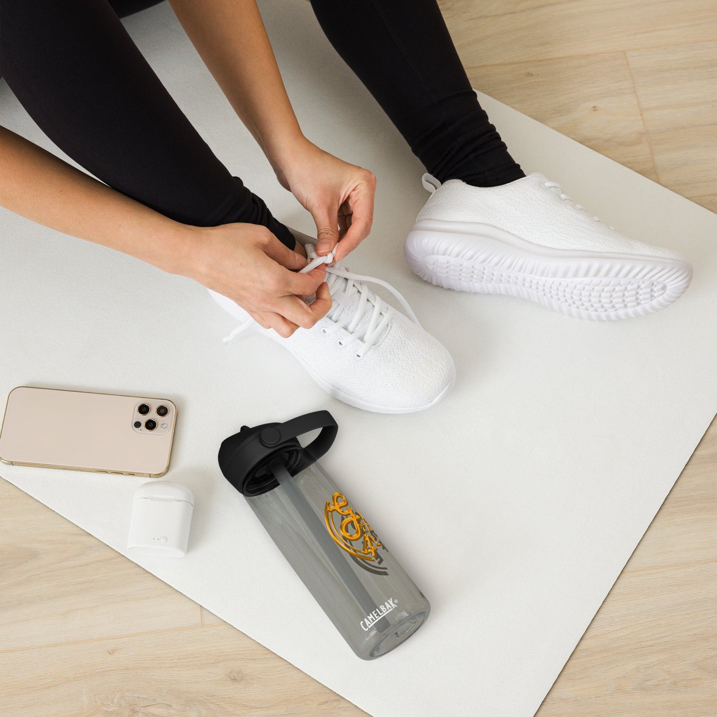 Person tying shoelaces on white sneakers with a phone and water bottle on a mat
