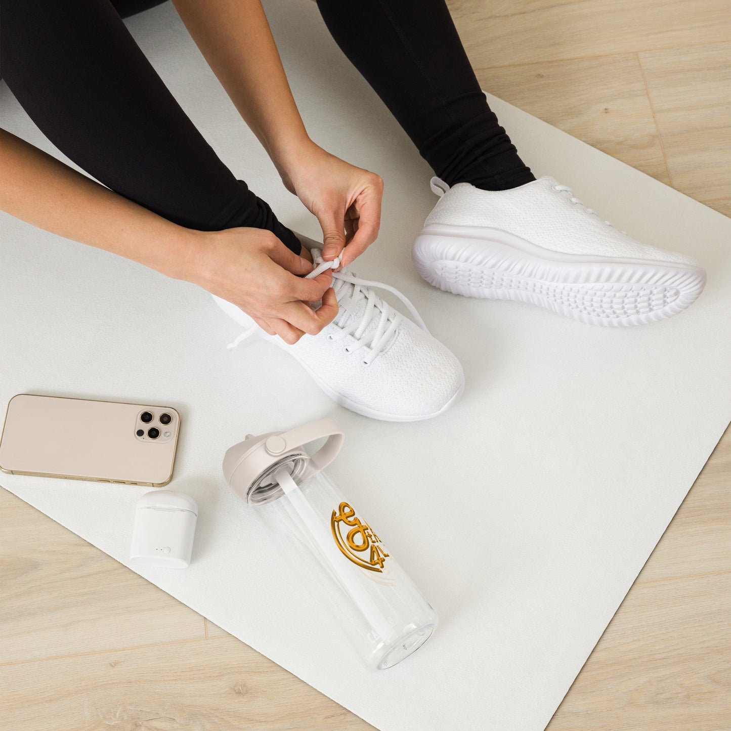 Person tying white sneakers on a white mat with a phone and water bottle nearby.