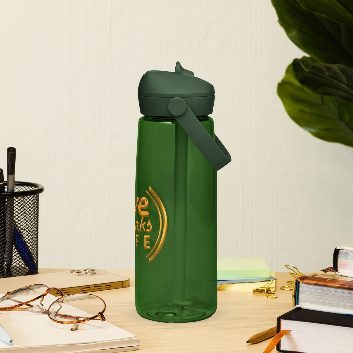 Green water bottle with text on a desk with glasses and books