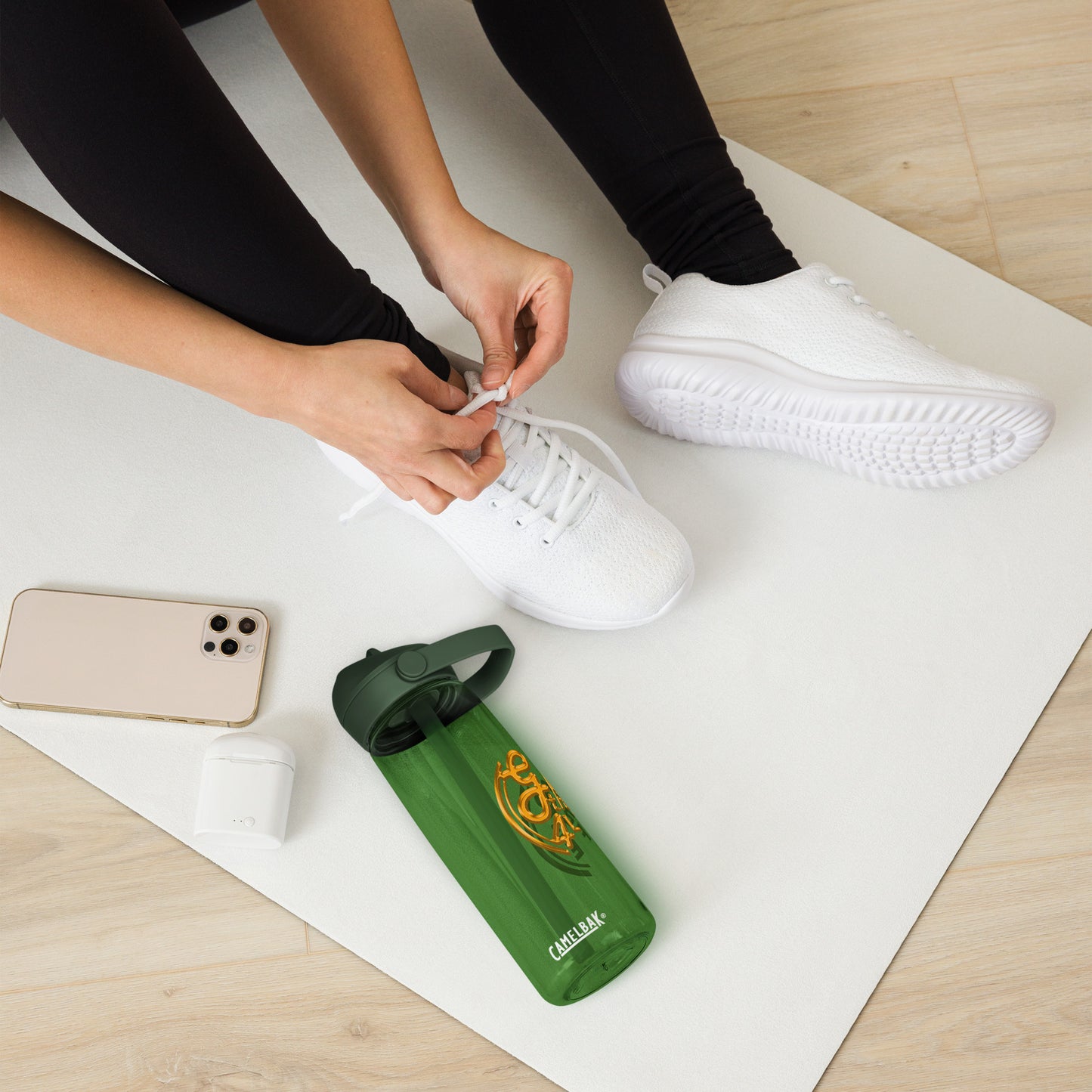 Person tying shoelaces on white sneakers with a green water bottle and phone on a white mat.