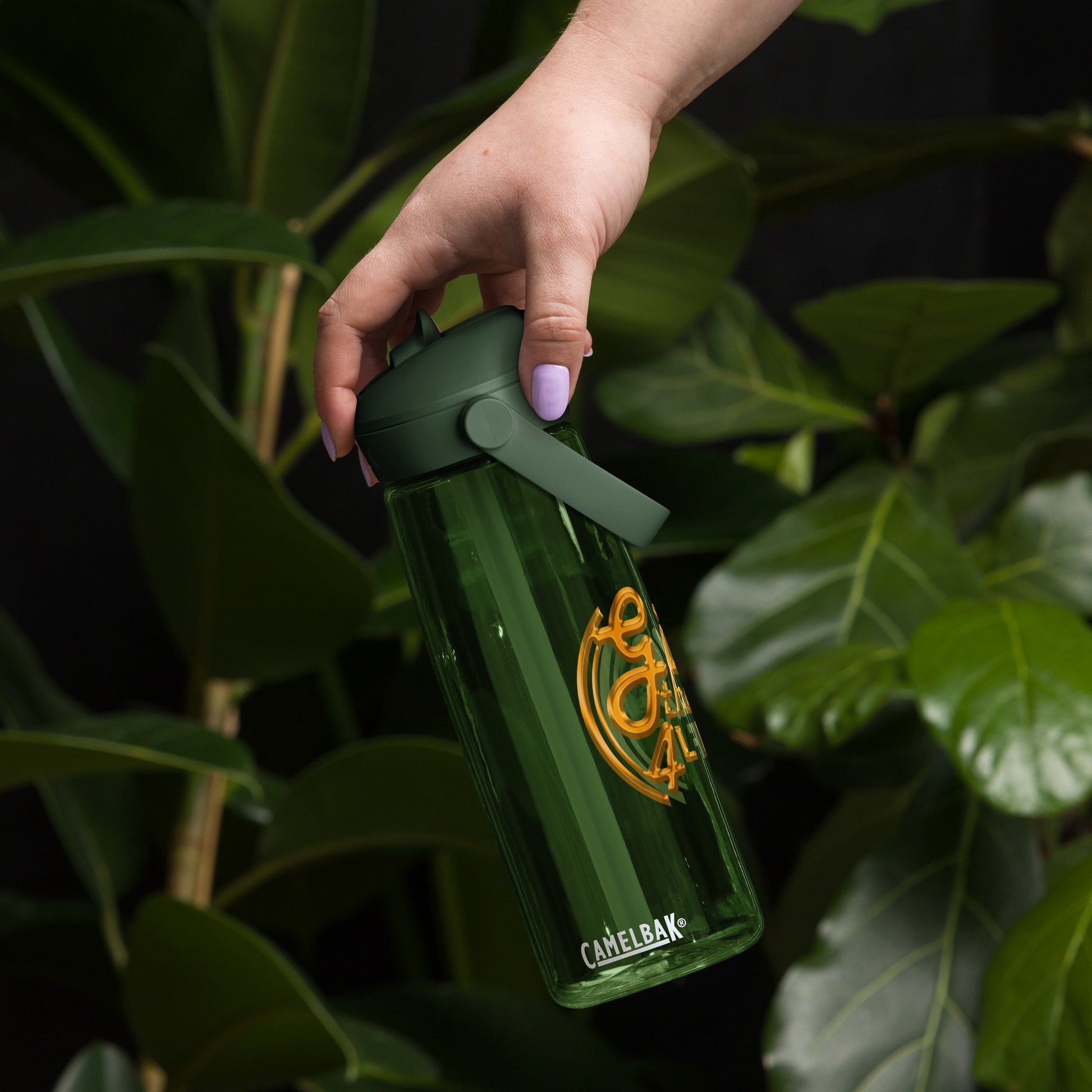 Hand holding a green CamelBak water bottle against a leafy background