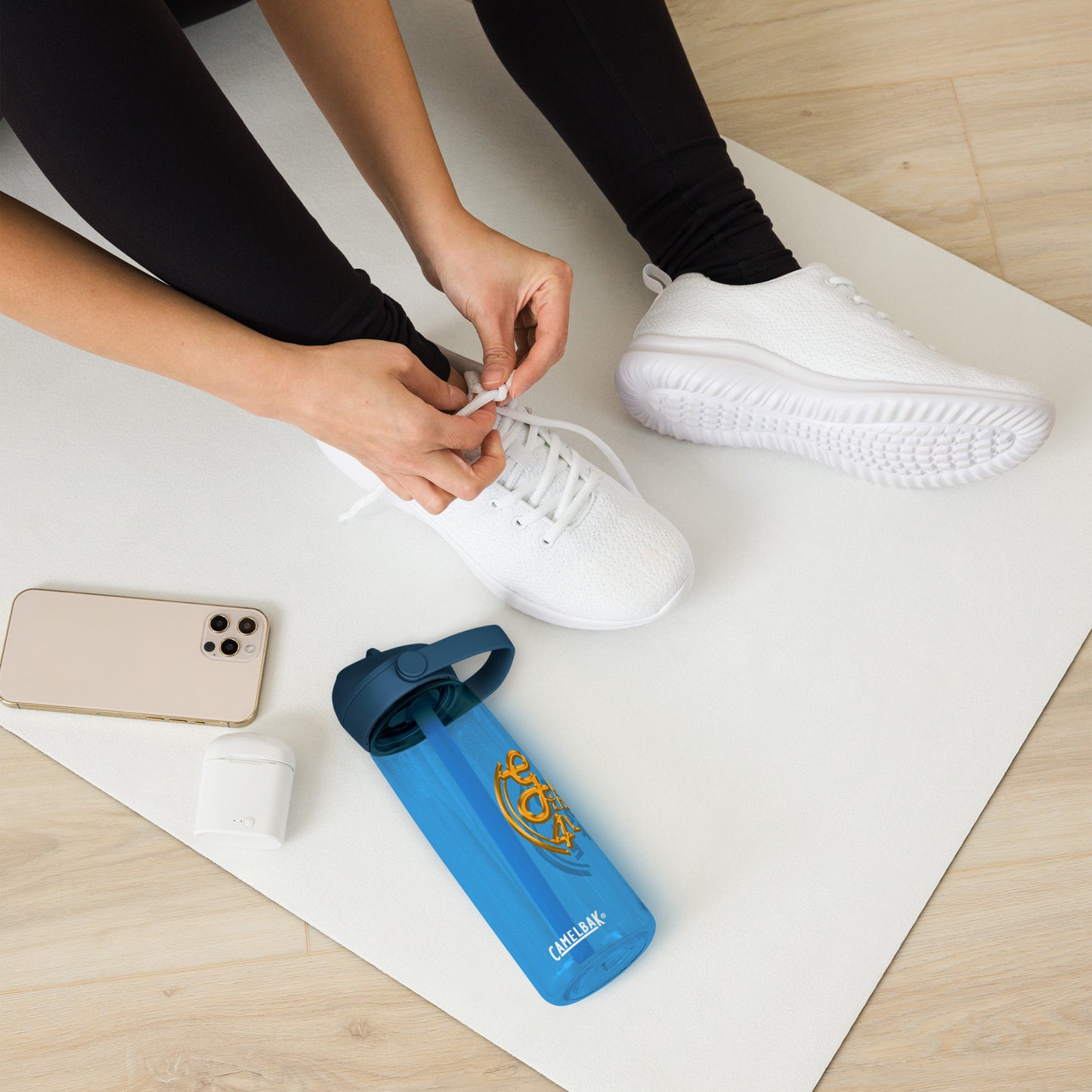 Person tying shoelaces on white sneakers with a blue water bottle and phone on a white mat.