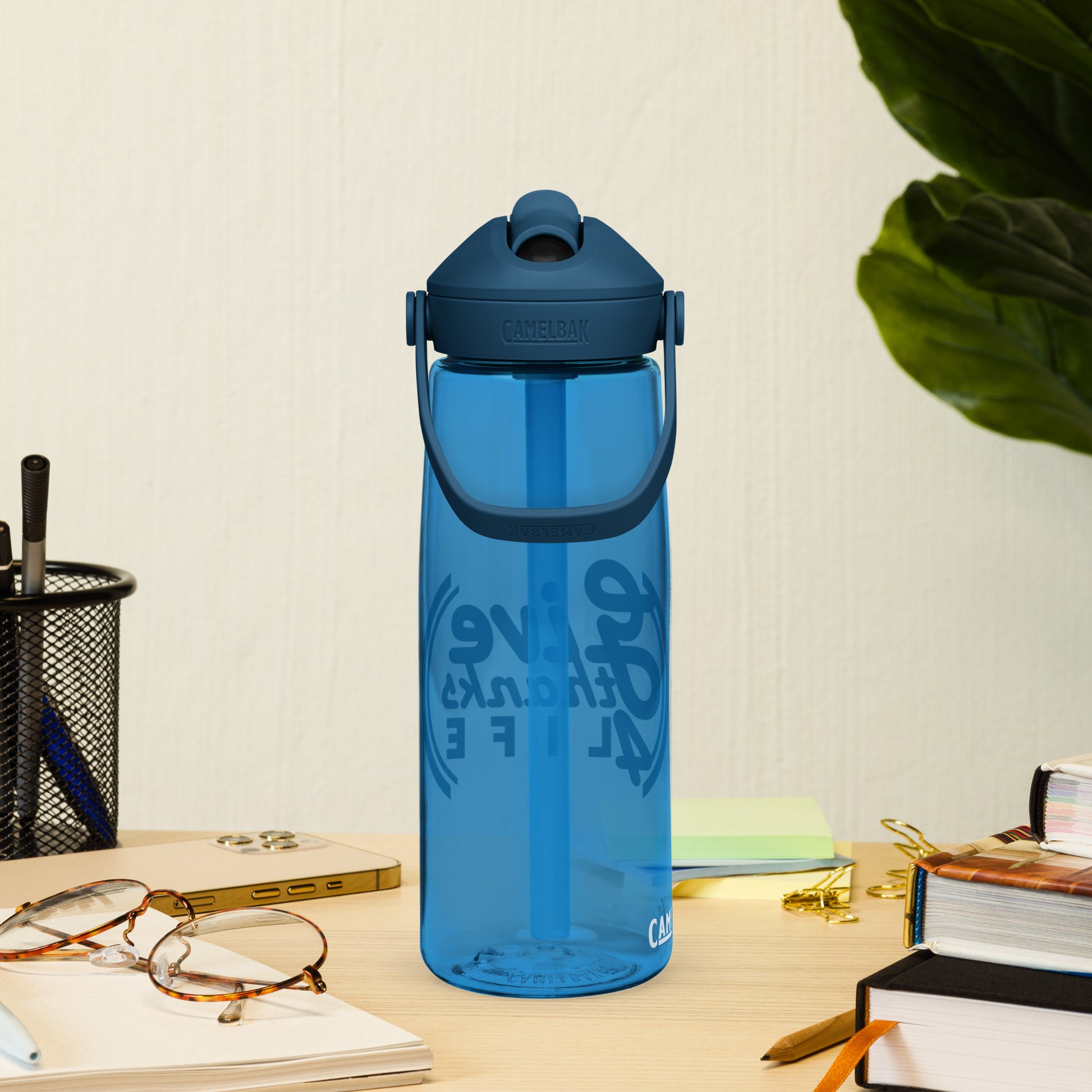 Blue water bottle with text on a desk with glasses, books, and a plant