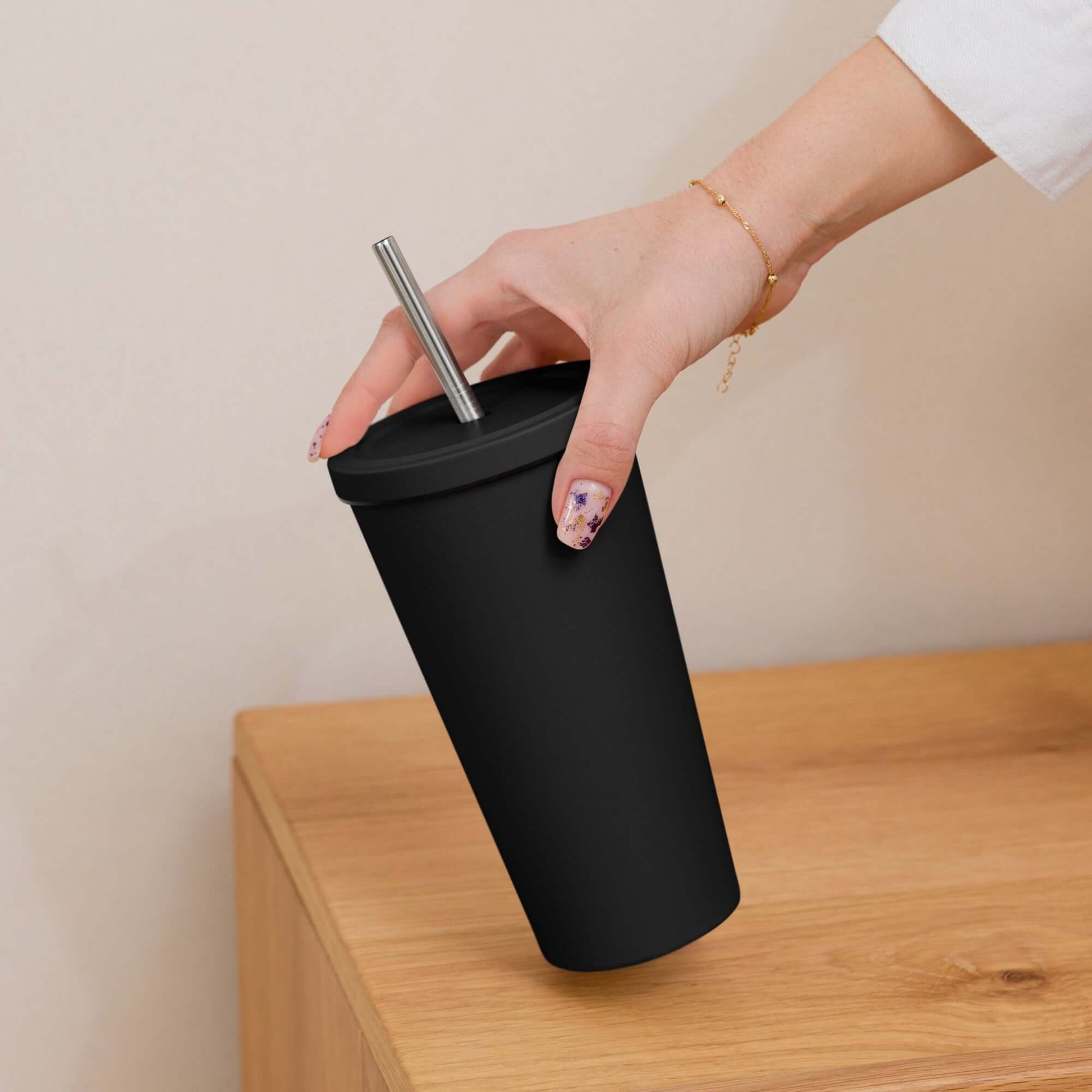 Hand holding a black tumbler with a straw on a wooden surface