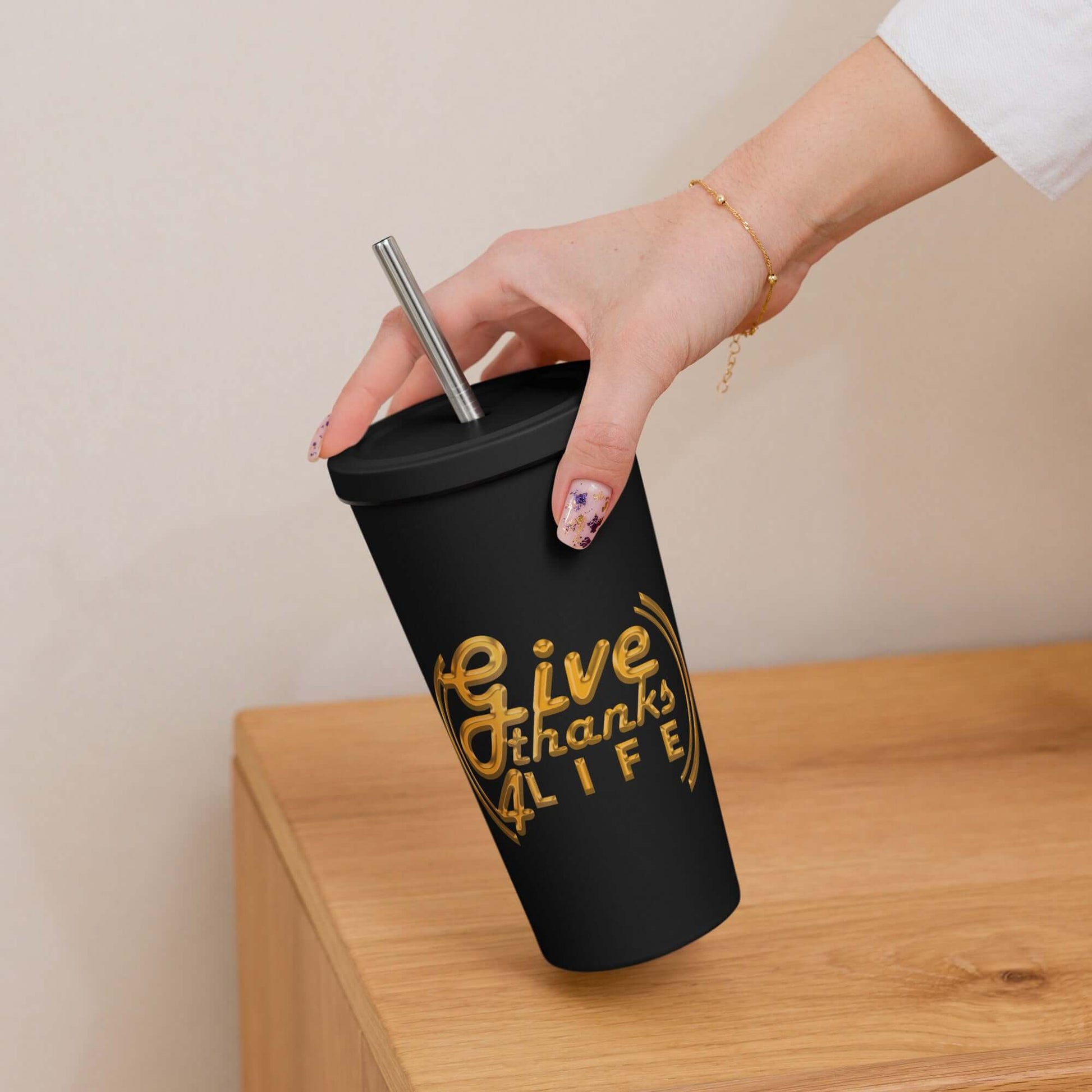 Black tumbler with gold text held by a hand on a wooden surface