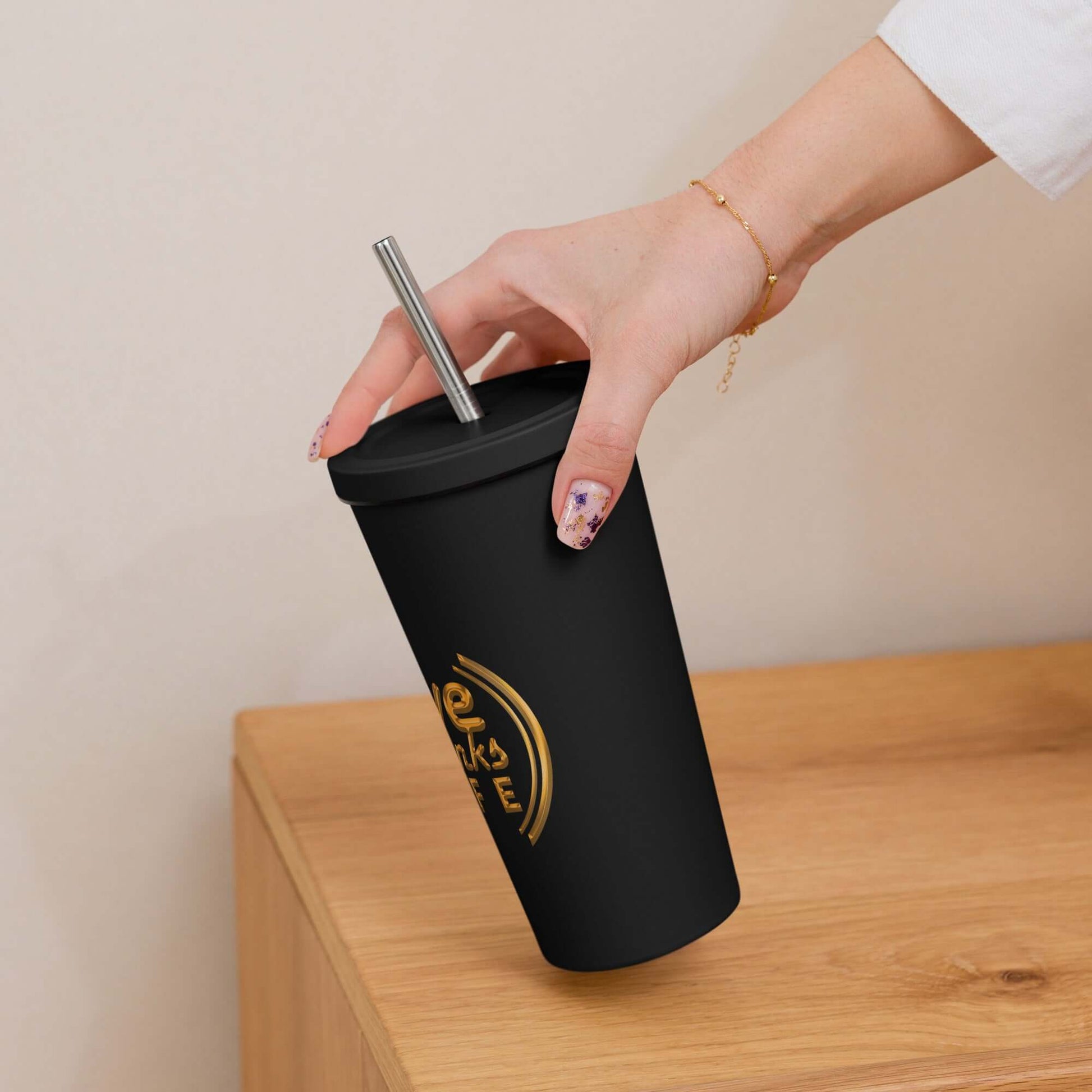Hand holding a black tumbler with a logo on a wooden surface