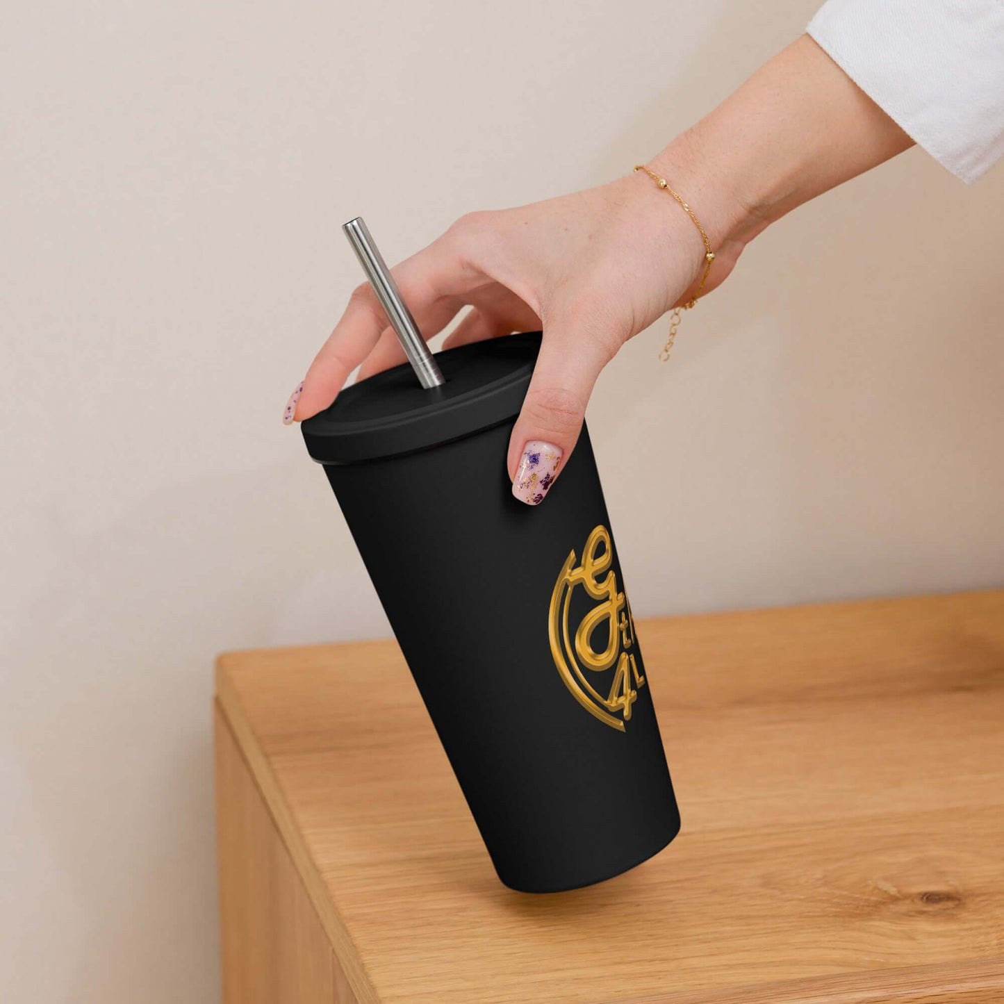 Hand holding a black tumbler with a gold logo on a wooden surface.
