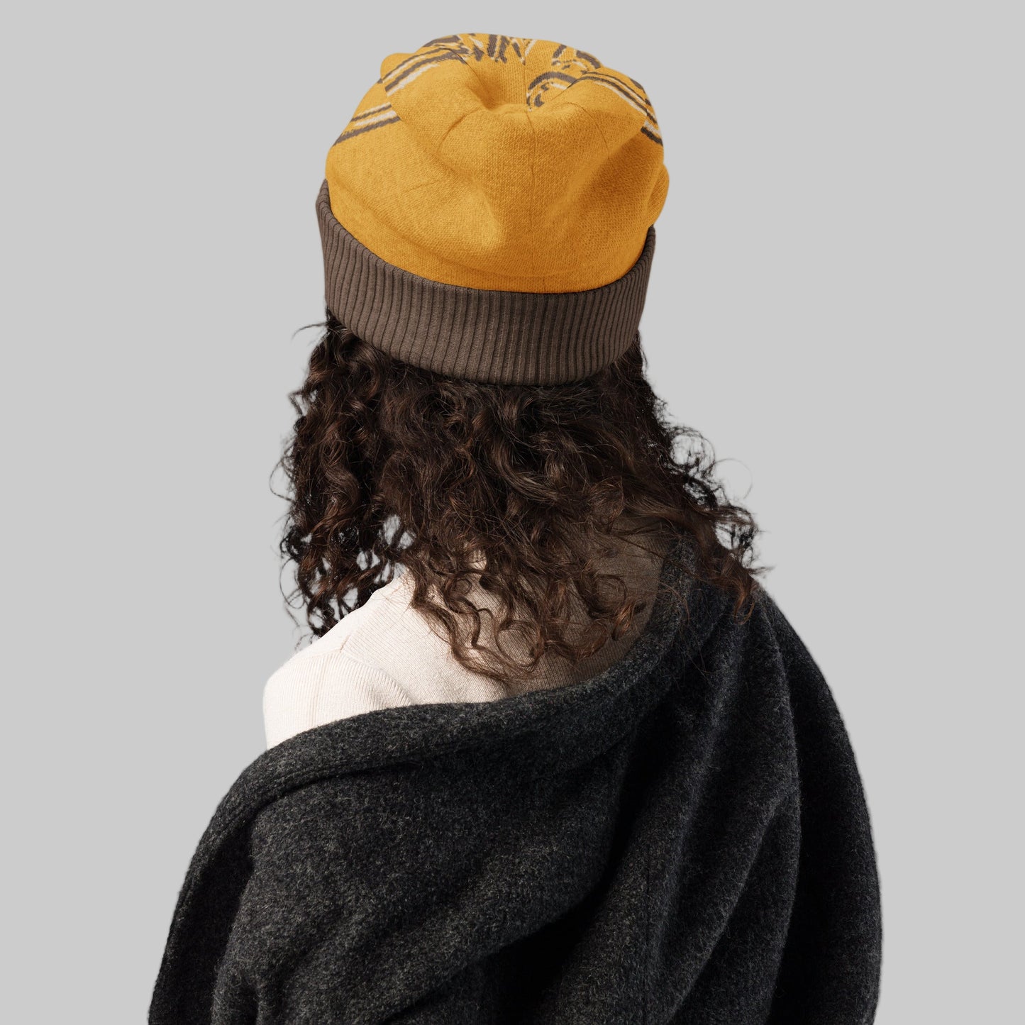 Person wearing a yellow and brown beanie with a dark coat on a white background
