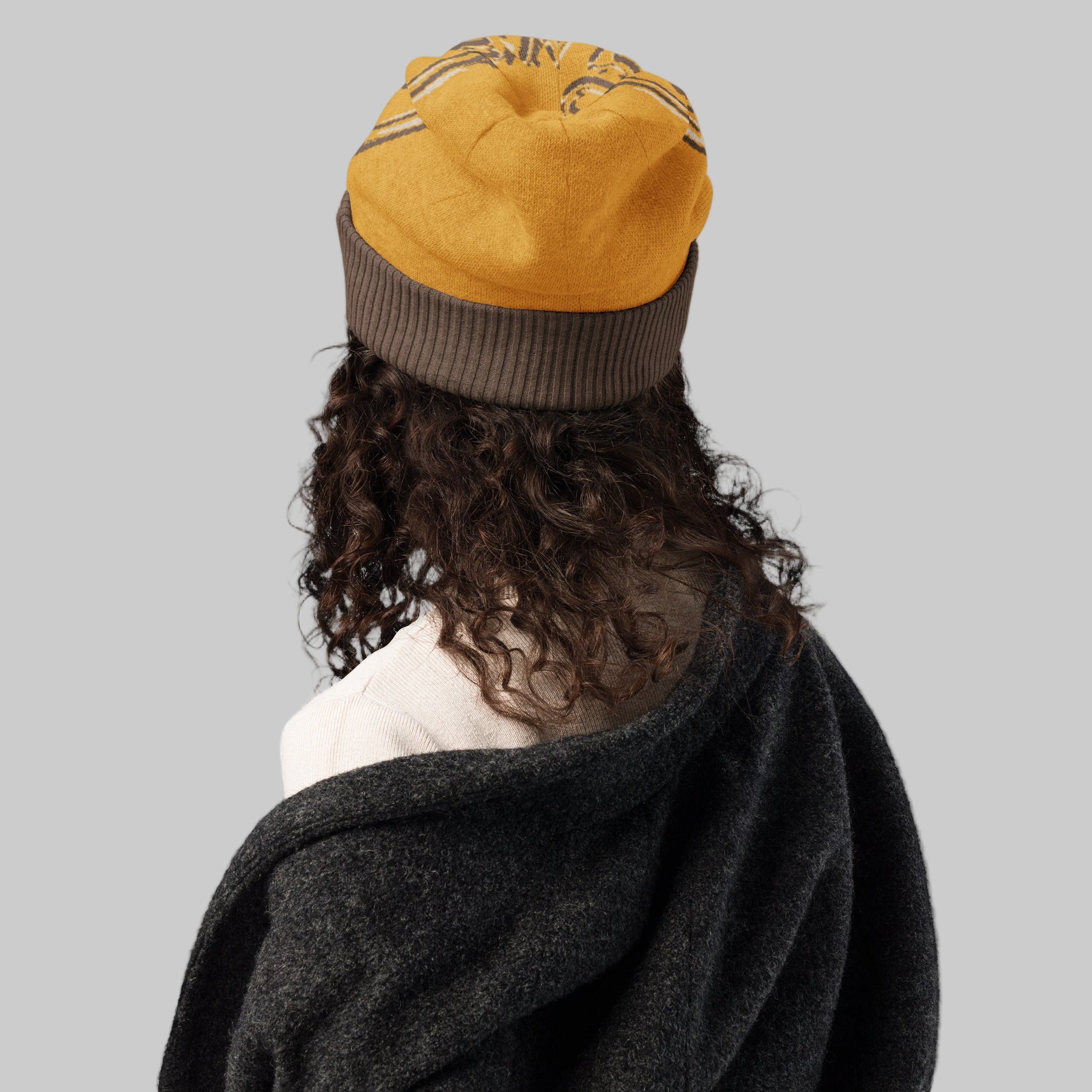 Person wearing a yellow and brown beanie with a dark coat on a white background
