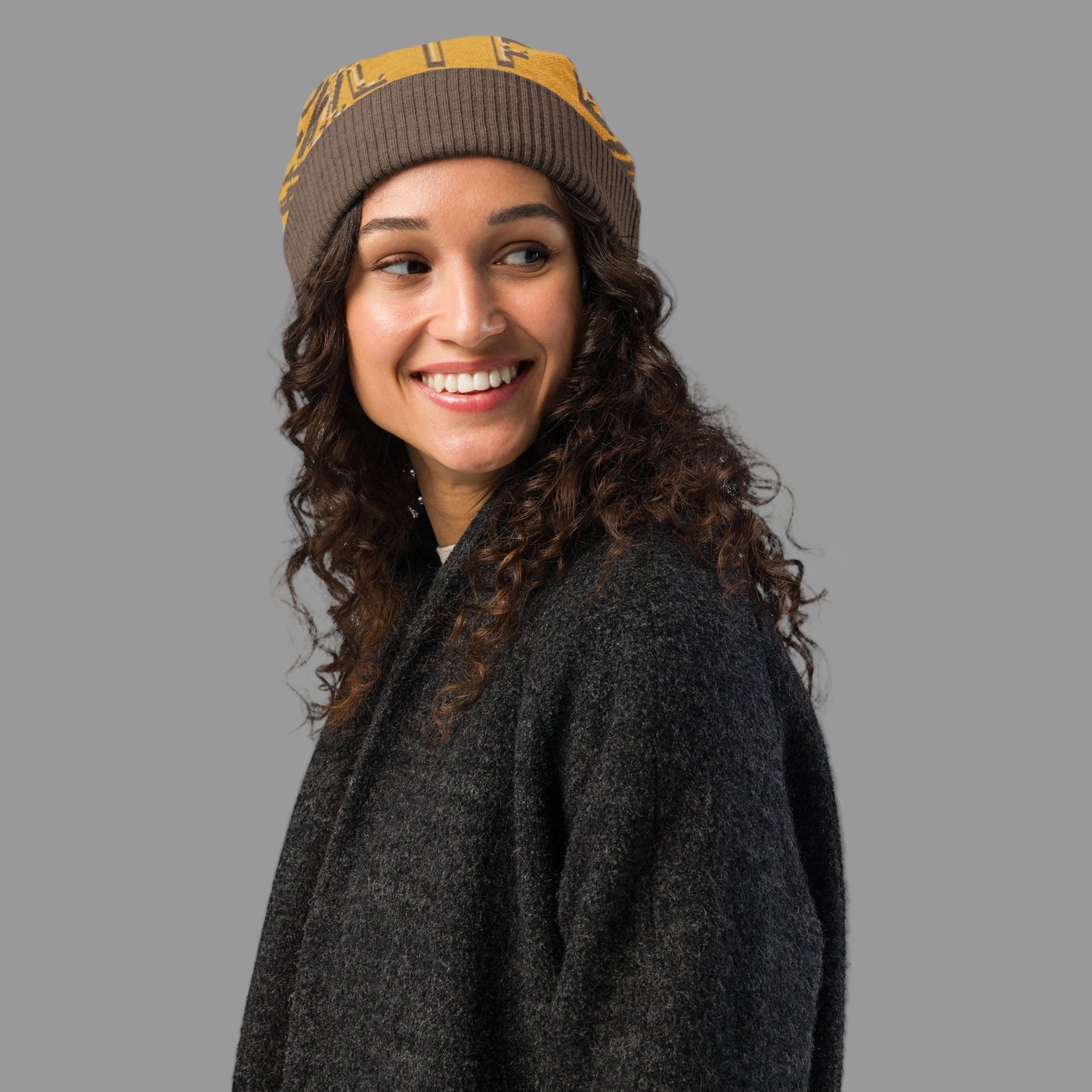 Woman wearing a brown and yellow beanie with a gray coat on a white background