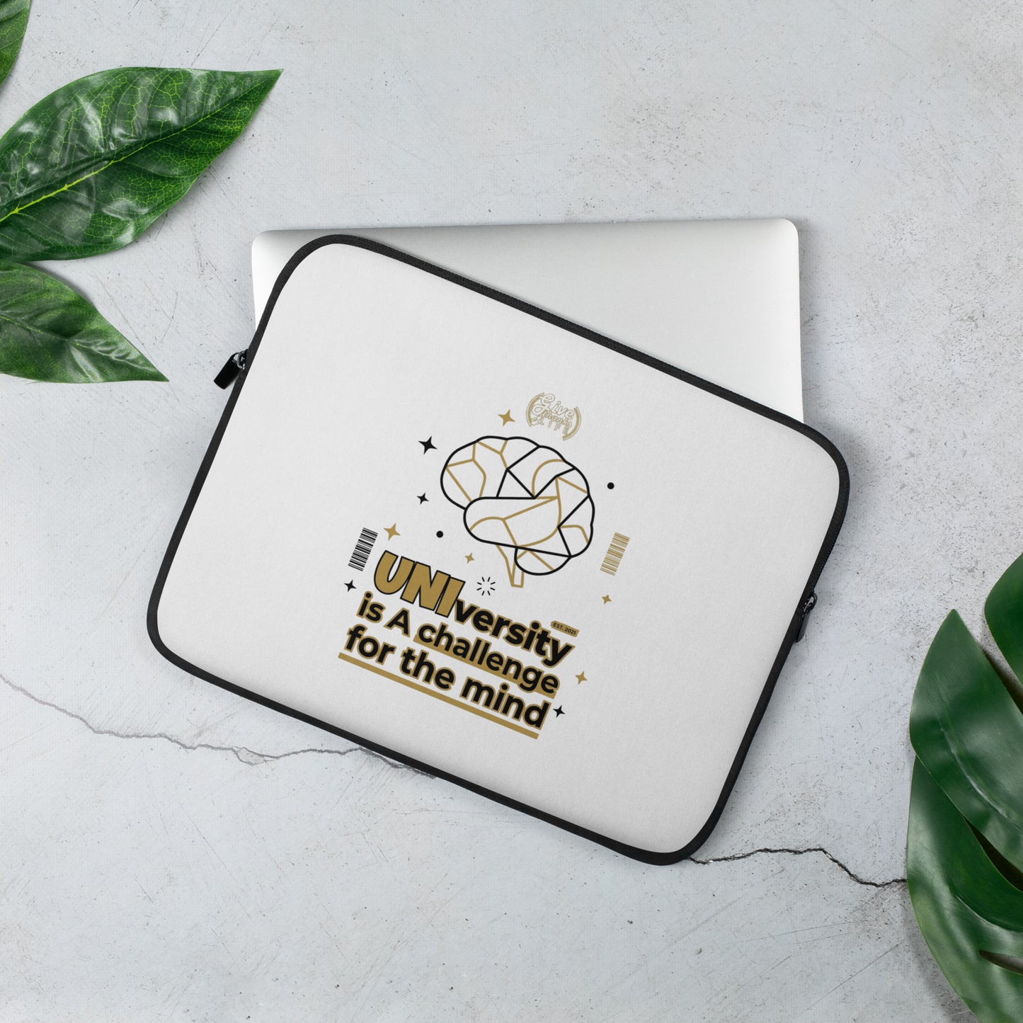 Laptop sleeve with brain graphic and text on a light gray surface with green leaves