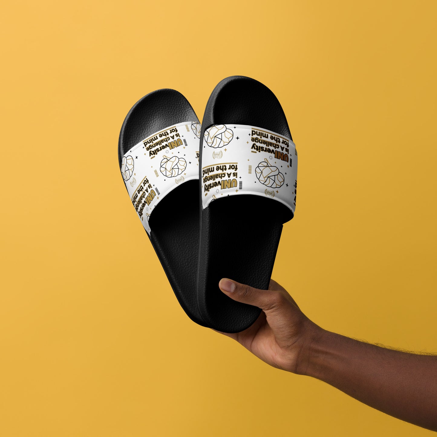 Black slides with white straps held by a hand against a yellow background