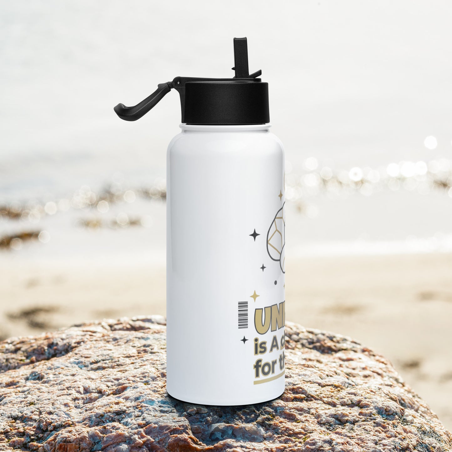 White water bottle with black lid on a rock by the beach