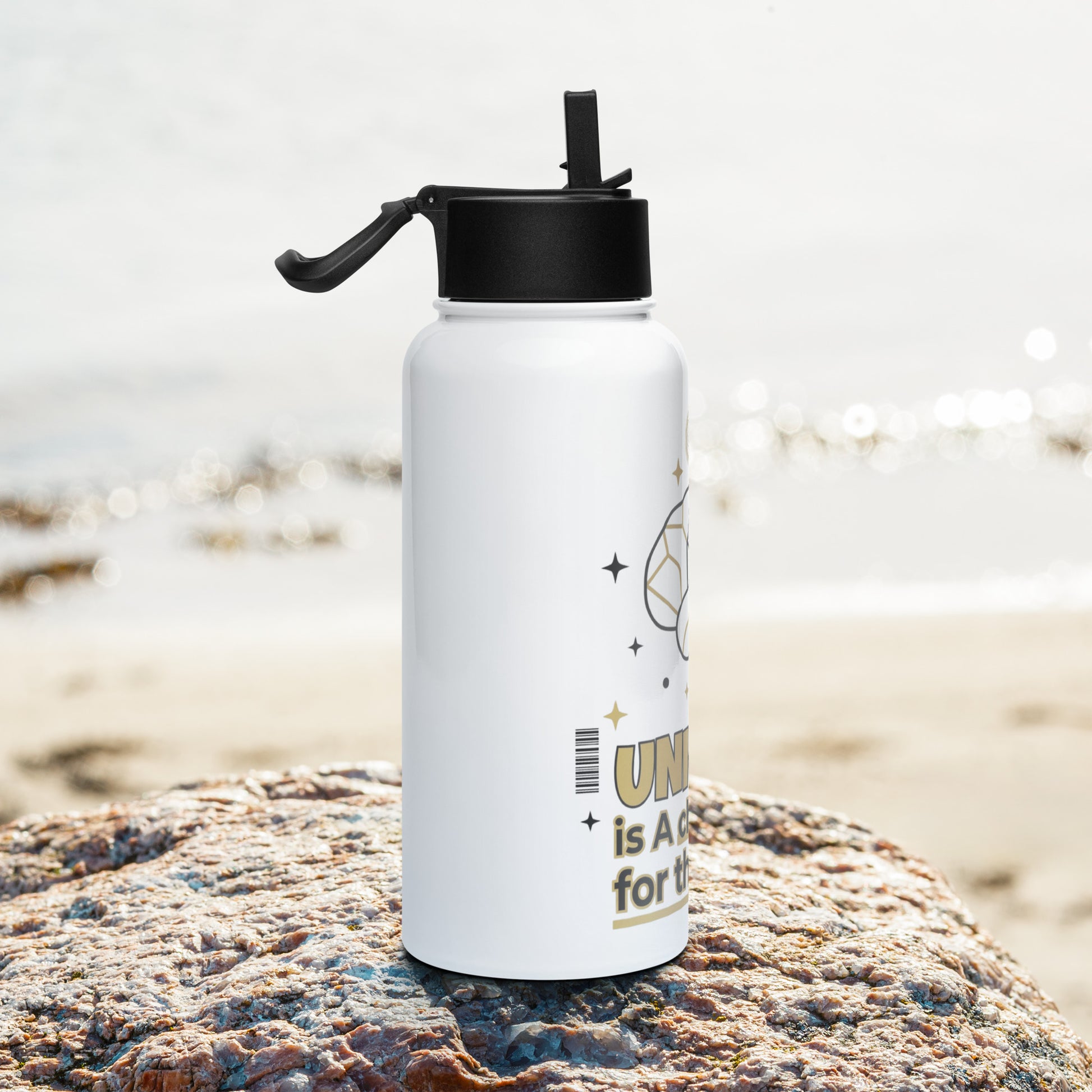 White water bottle with black lid on a rock by the beach