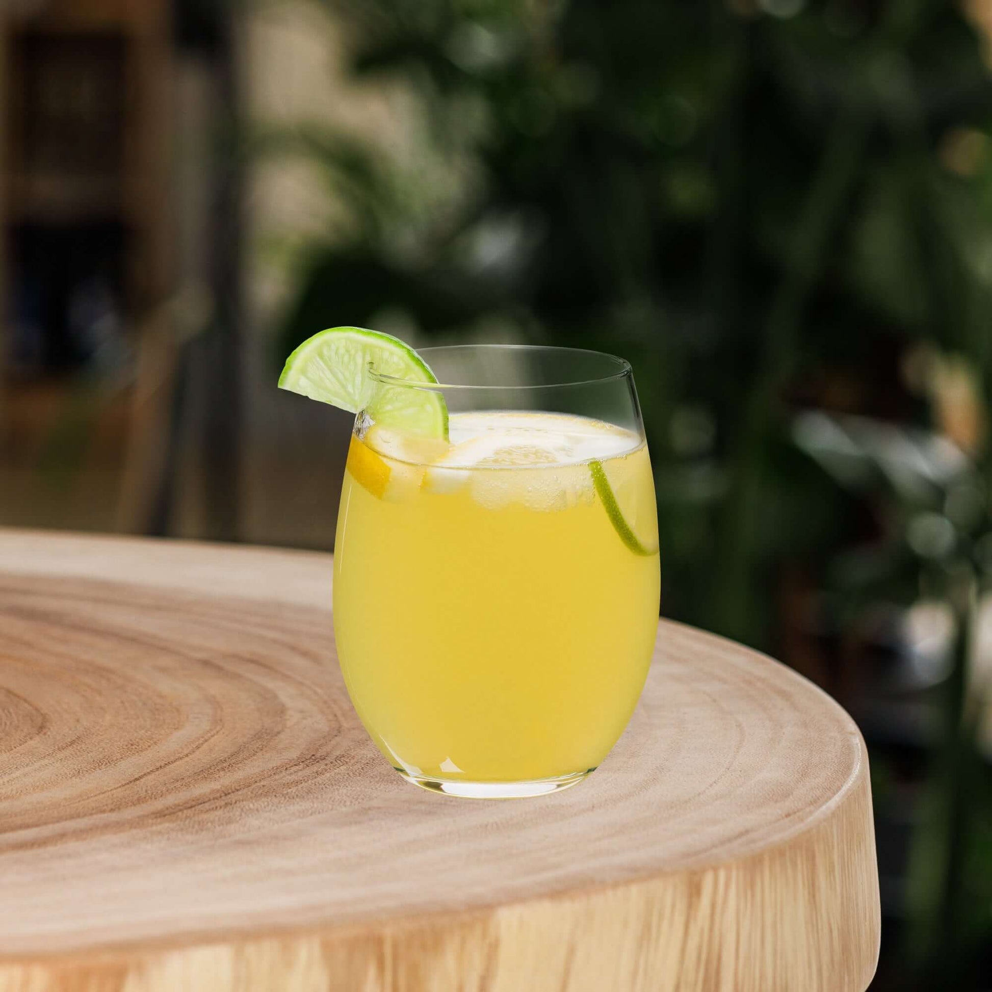 Glass of yellow drink with lime slices on a wooden surface