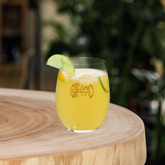 Glass of yellow drink with lime slices on a wooden surface, featuring 'Give Thanks' text.