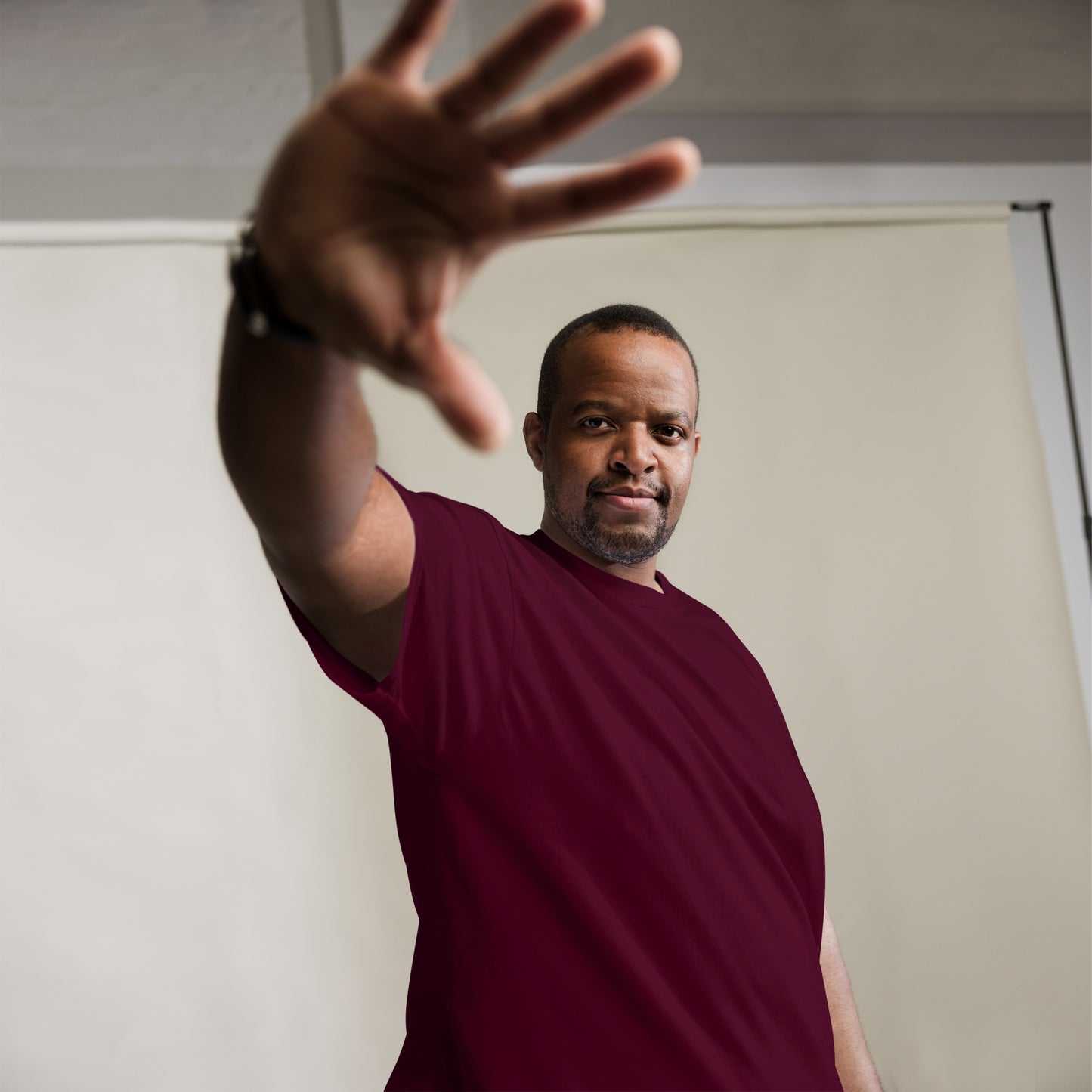 Man in a red shirt extending his hand towards the camera with a neutral background