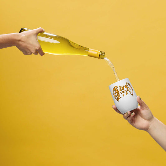 Person pouring white wine from a bottle into a white tumbler with 'Live Laugh Love' text on a yellow background