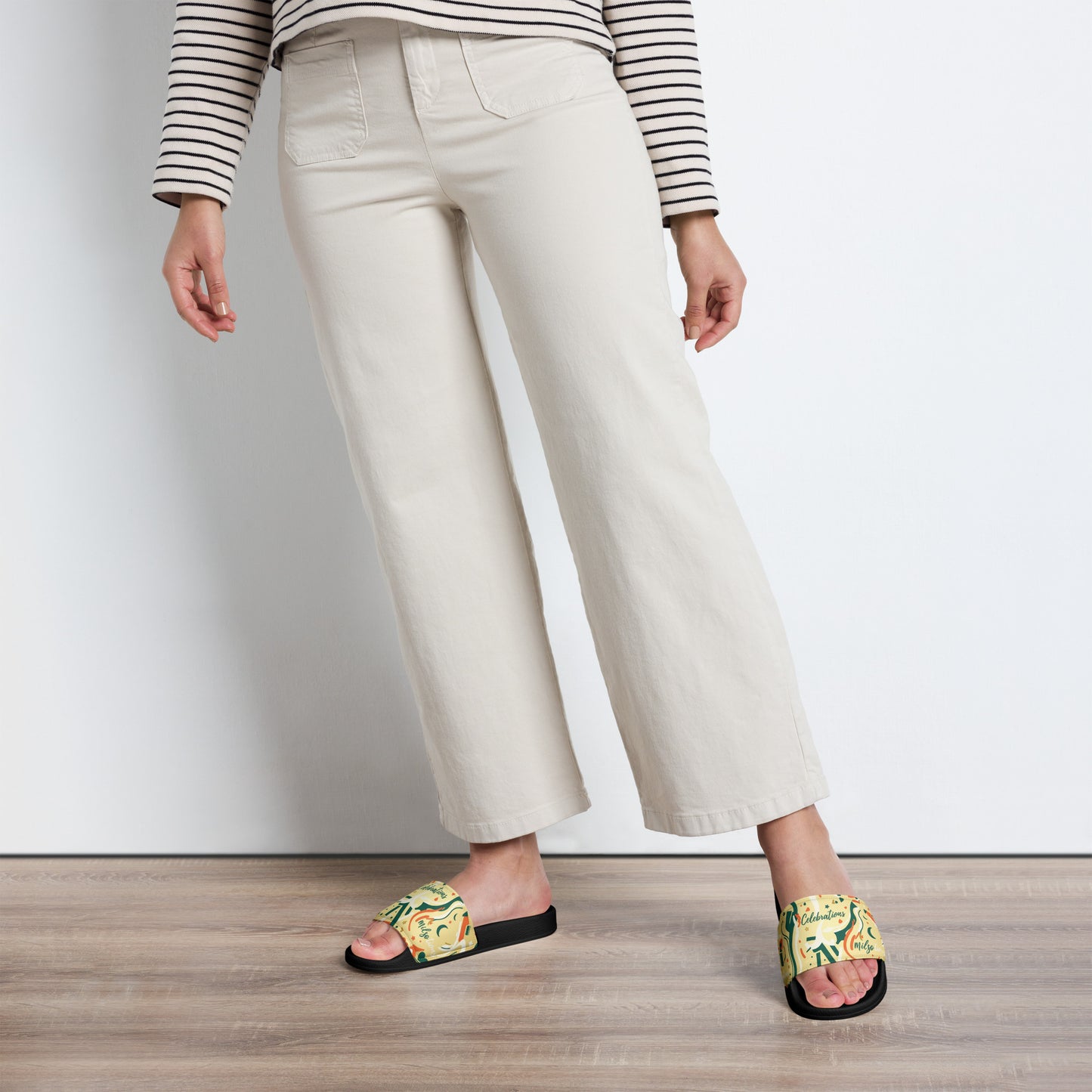Person wearing white pants and colorful sandals on a wooden floor.