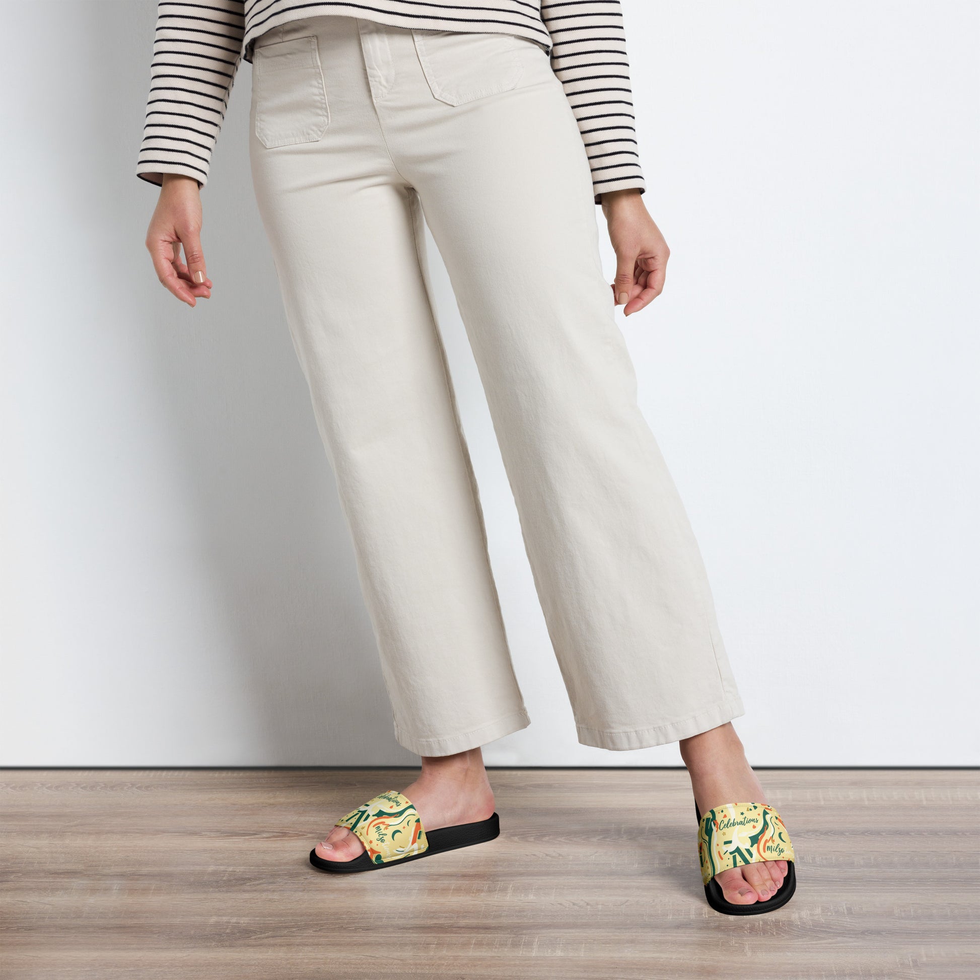 Person wearing white pants and colorful sandals on a wooden floor.