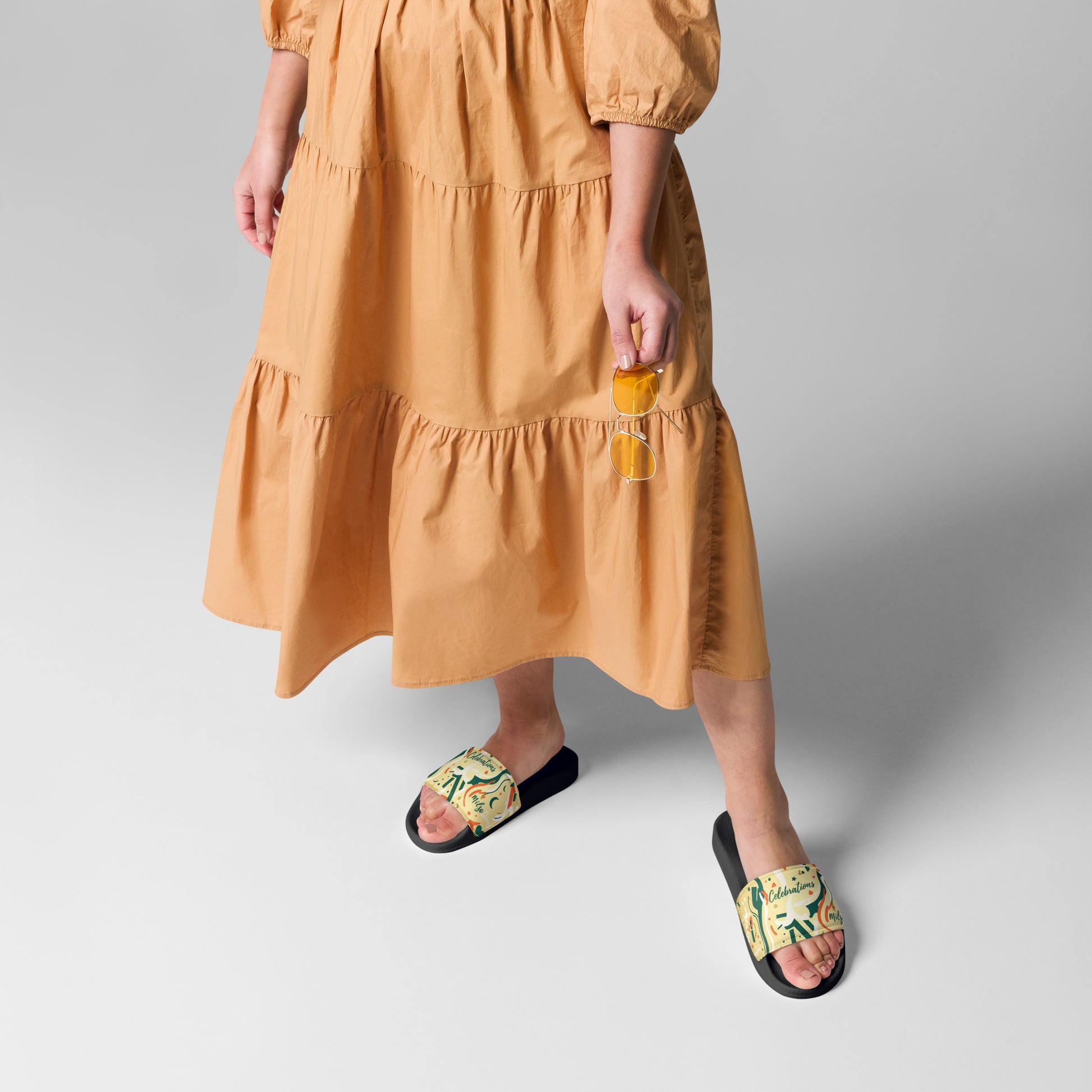 Person wearing a mustard yellow dress and black sandals with gold accents on a light gray background