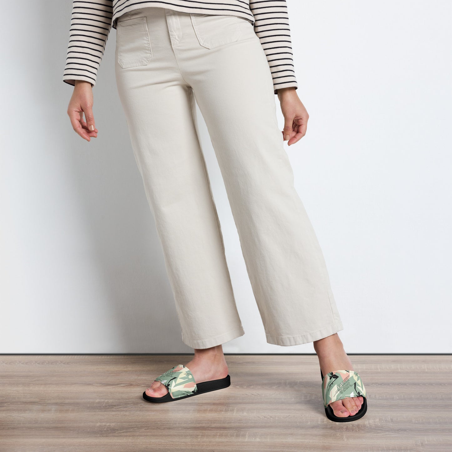 Person wearing white pants and floral sandals on a wooden floor.