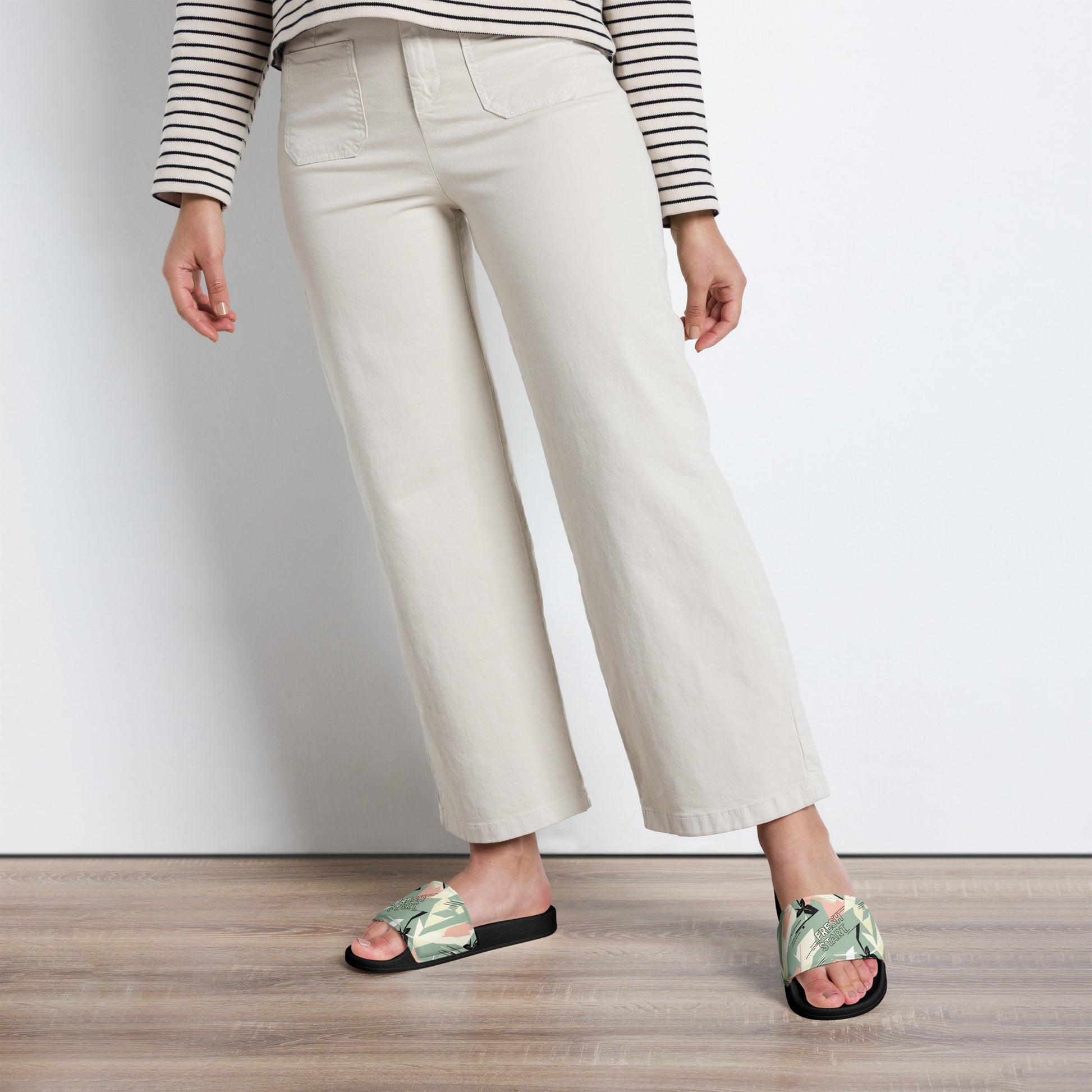 Person wearing white pants and floral sandals on a wooden floor.