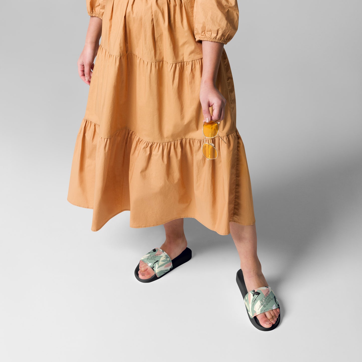 Person wearing a mustard yellow dress and black floral sandals on a light gray background