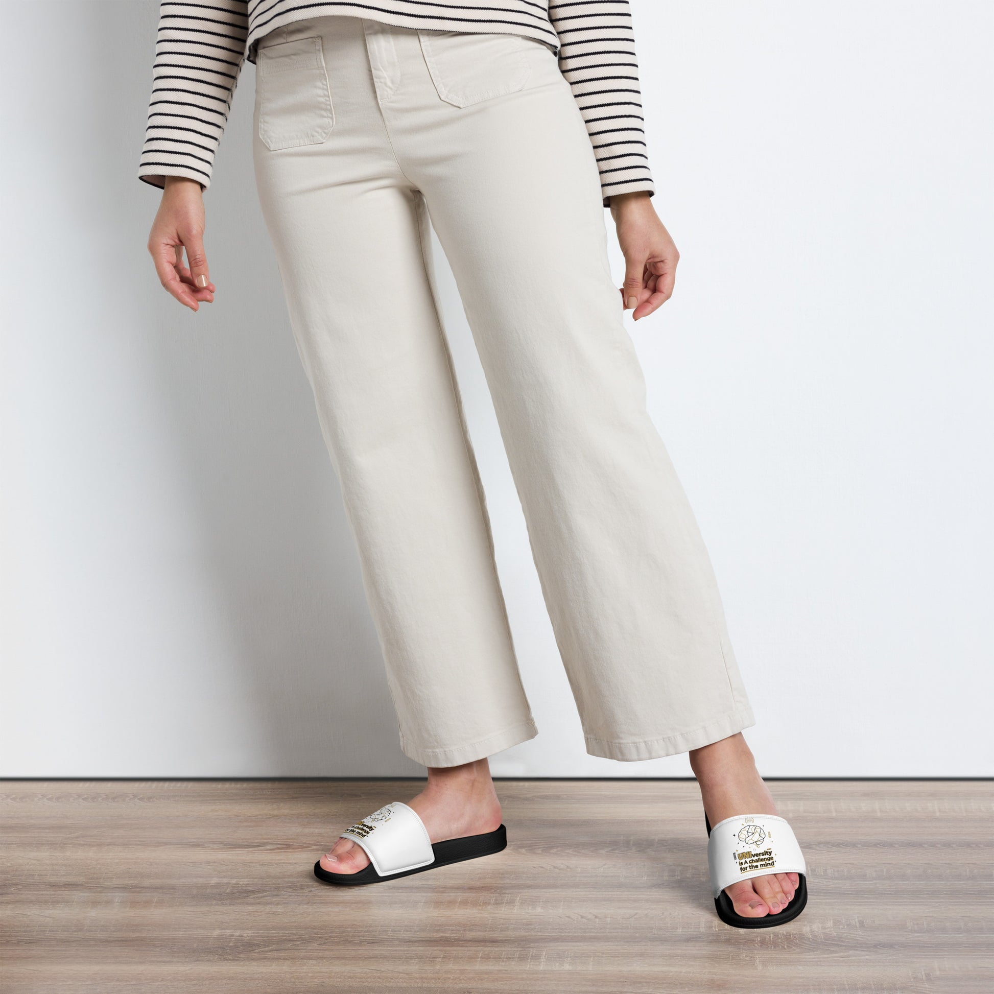 Person wearing white slides with text, beige pants, and a striped shirt on a plain background