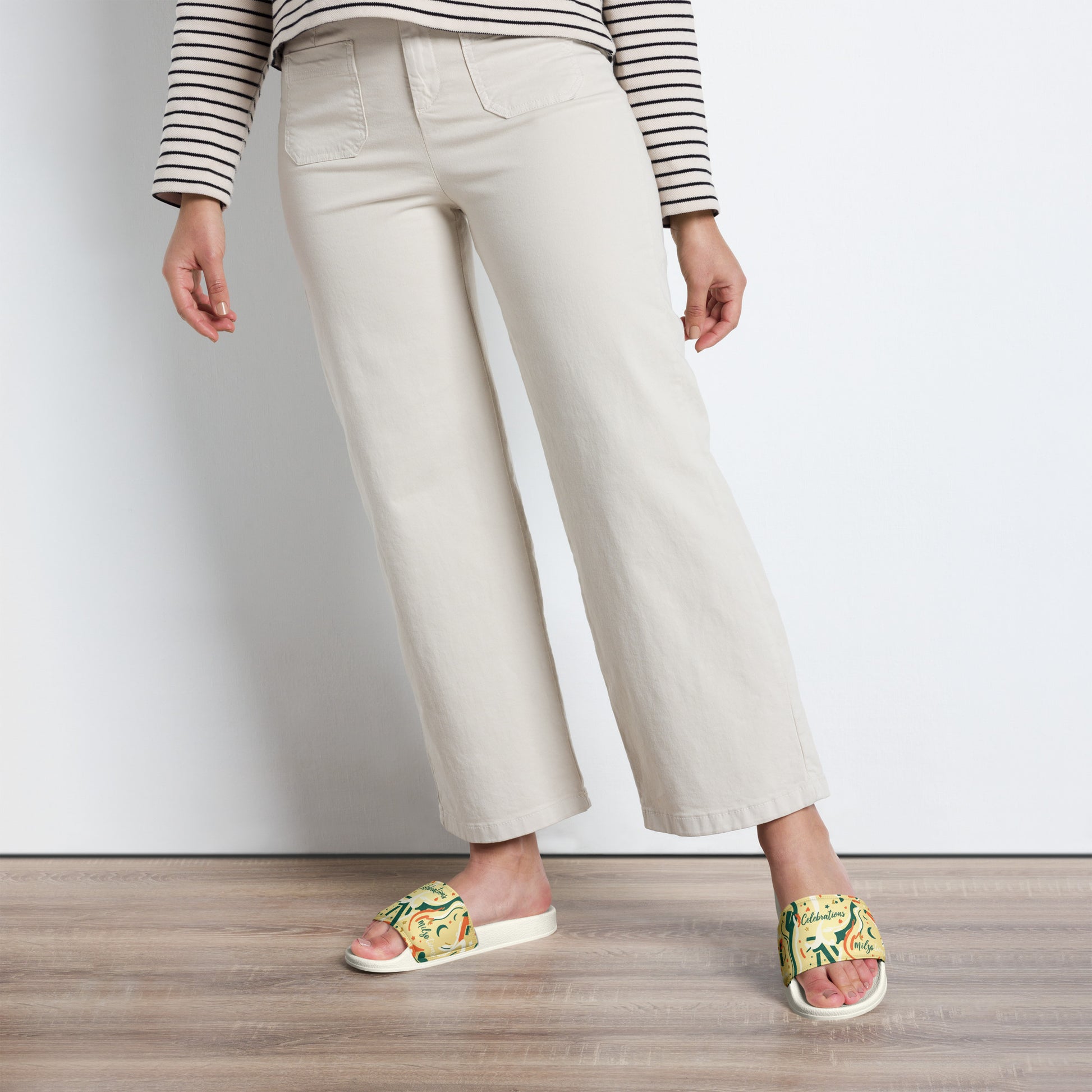Person wearing beige pants and colorful sandals on a wooden floor.