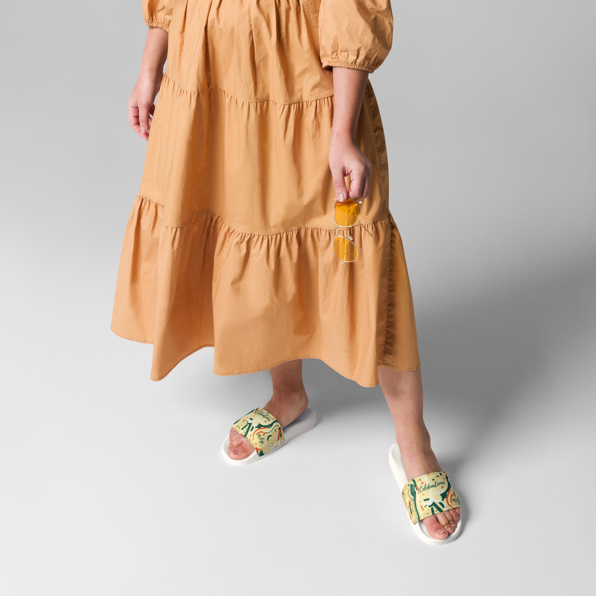 Person wearing a mustard yellow dress with floral sandals on a light gray background