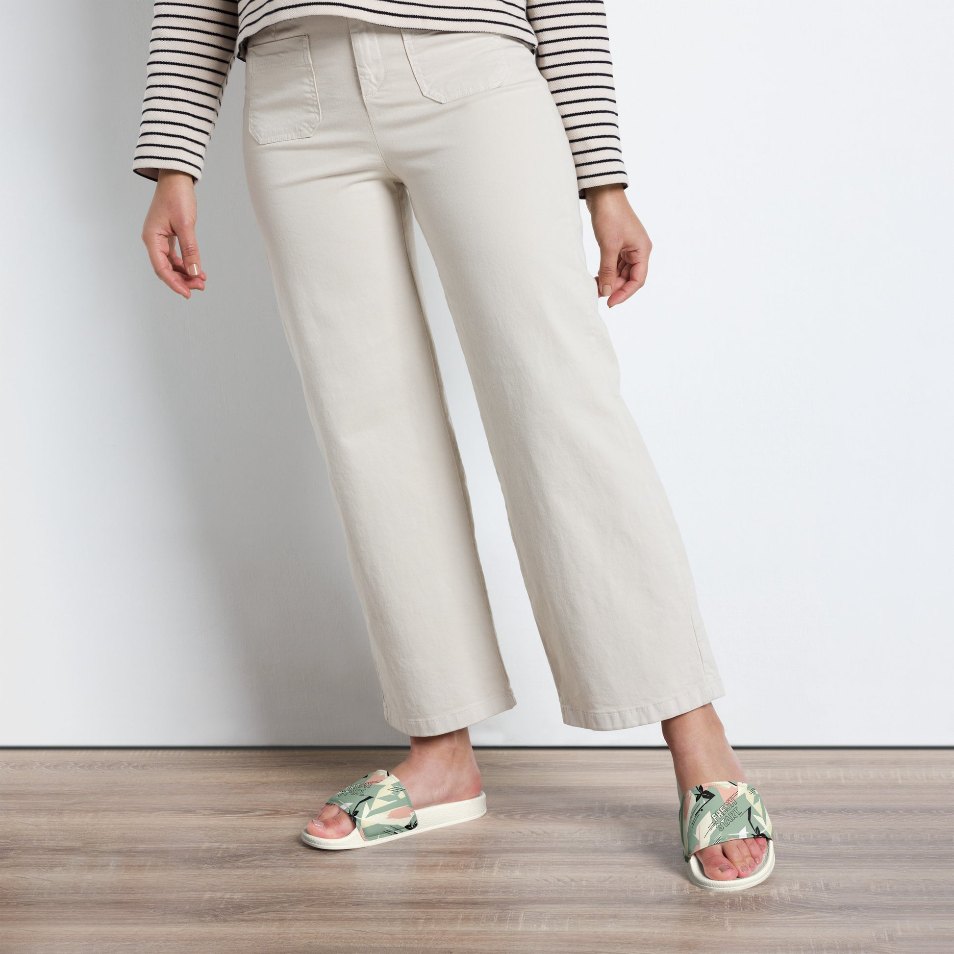 Person wearing light-colored pants and floral sandals on a wooden floor.